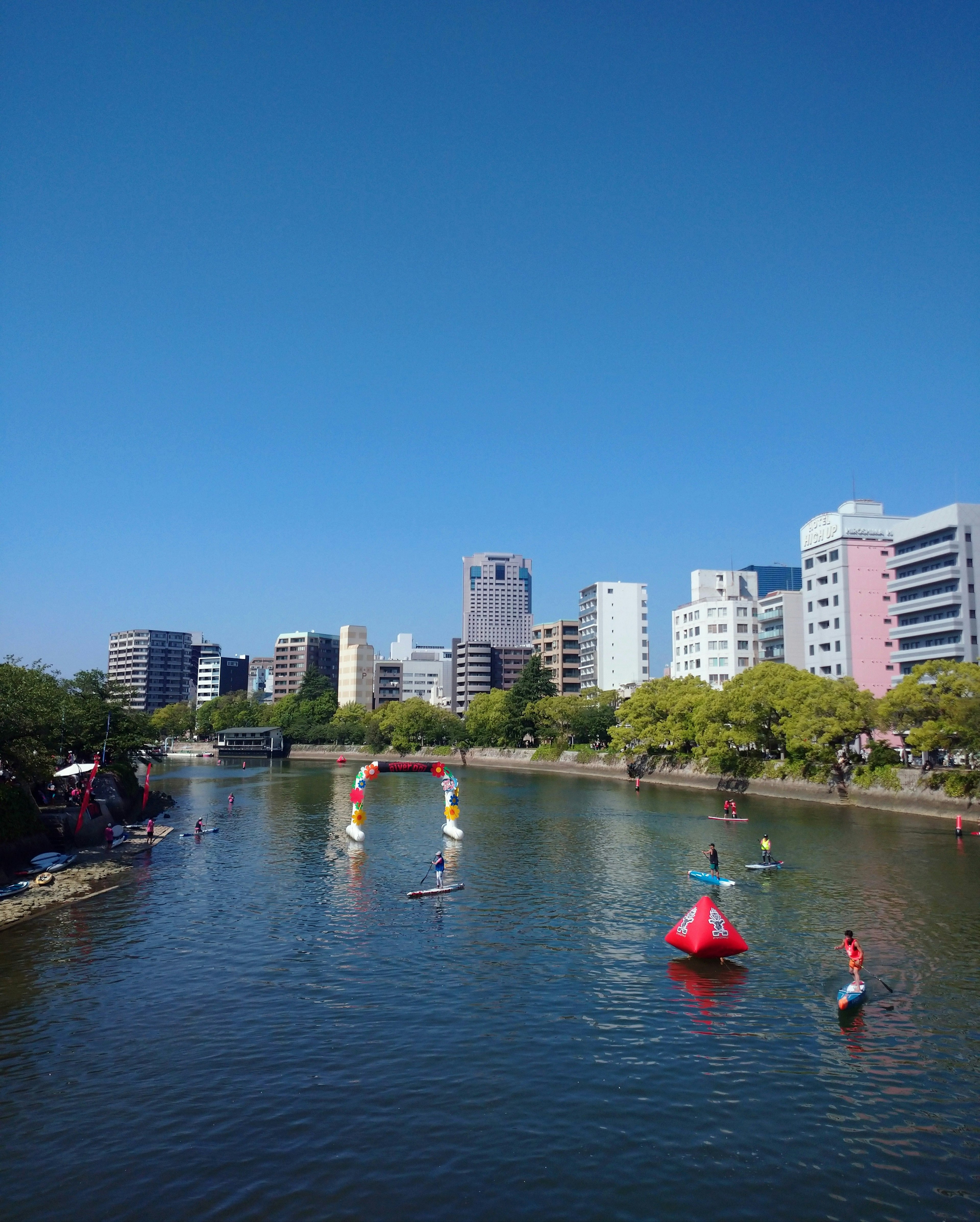 Personas disfrutando del paddle surf bajo un cielo azul con el horizonte de la ciudad