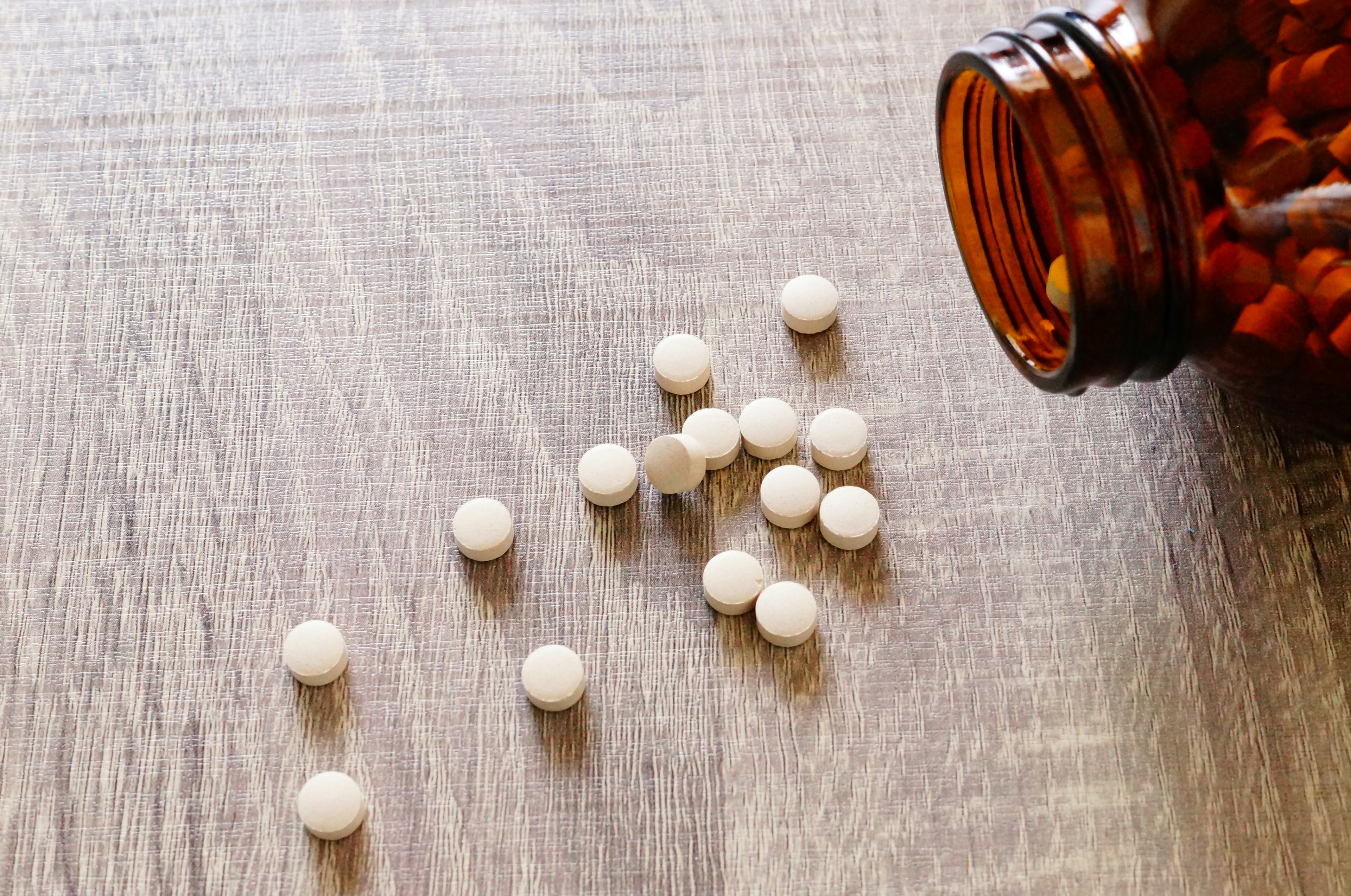 Weiße runde Tabletten, die aus einer braunen Flasche auf einen Holztisch gefallen sind