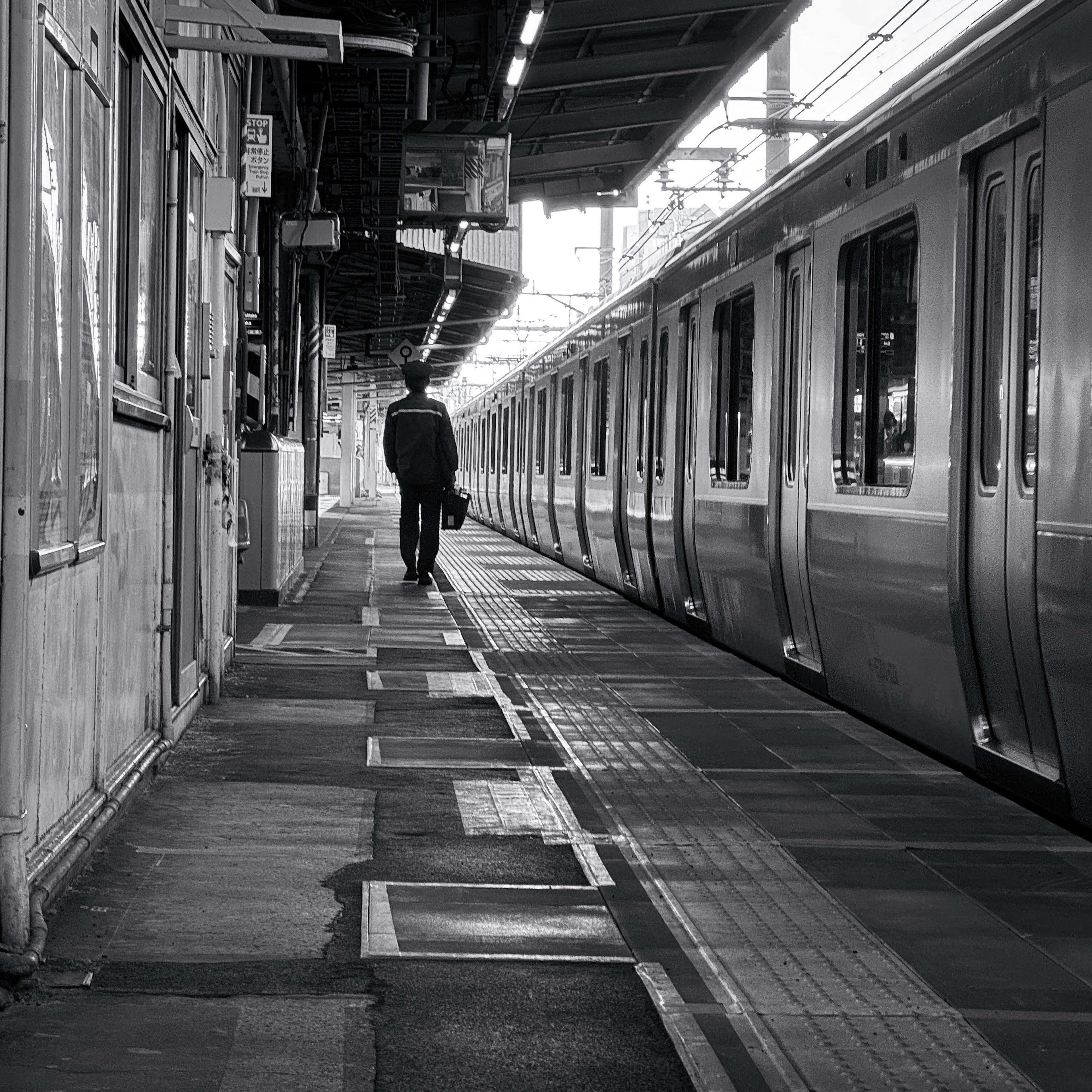 白黒の駅で電車のホームを歩く男性