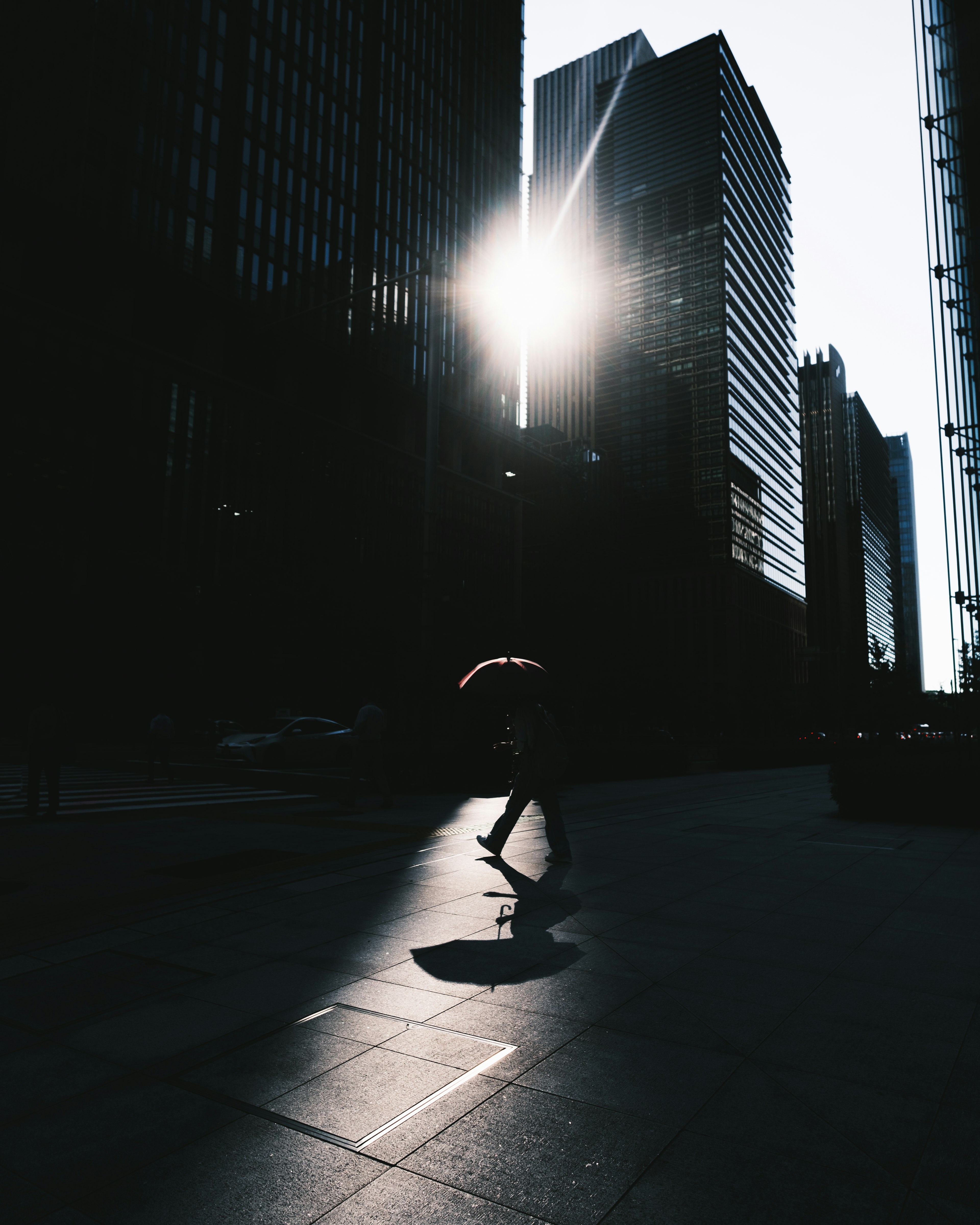 Silhouette einer Person mit einem Regenschirm, die zwischen Gebäuden geht, mit Sonnenlicht im Hintergrund