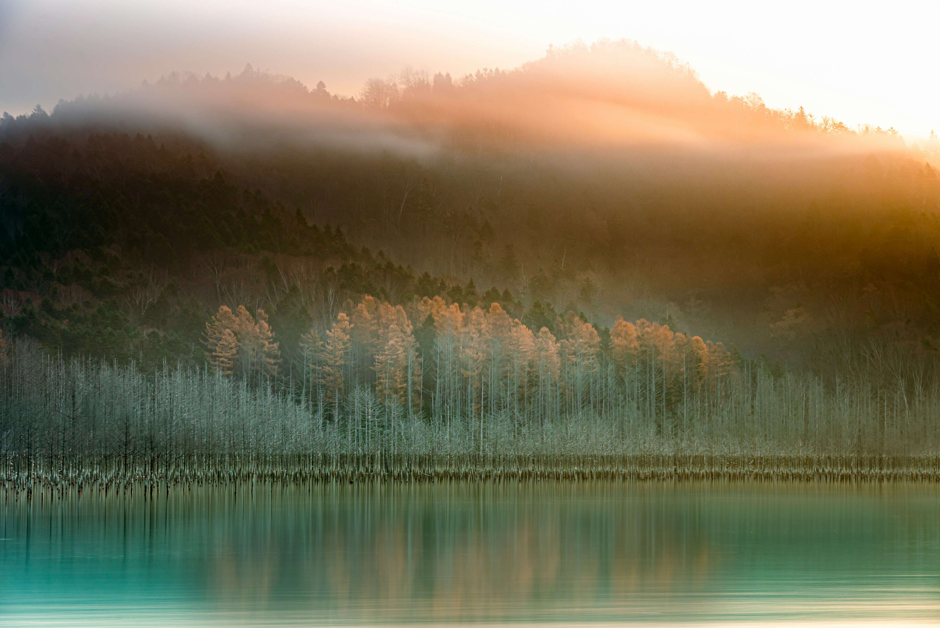 Misty mountains and tranquil lake landscape Soft morning light reflecting on the hills