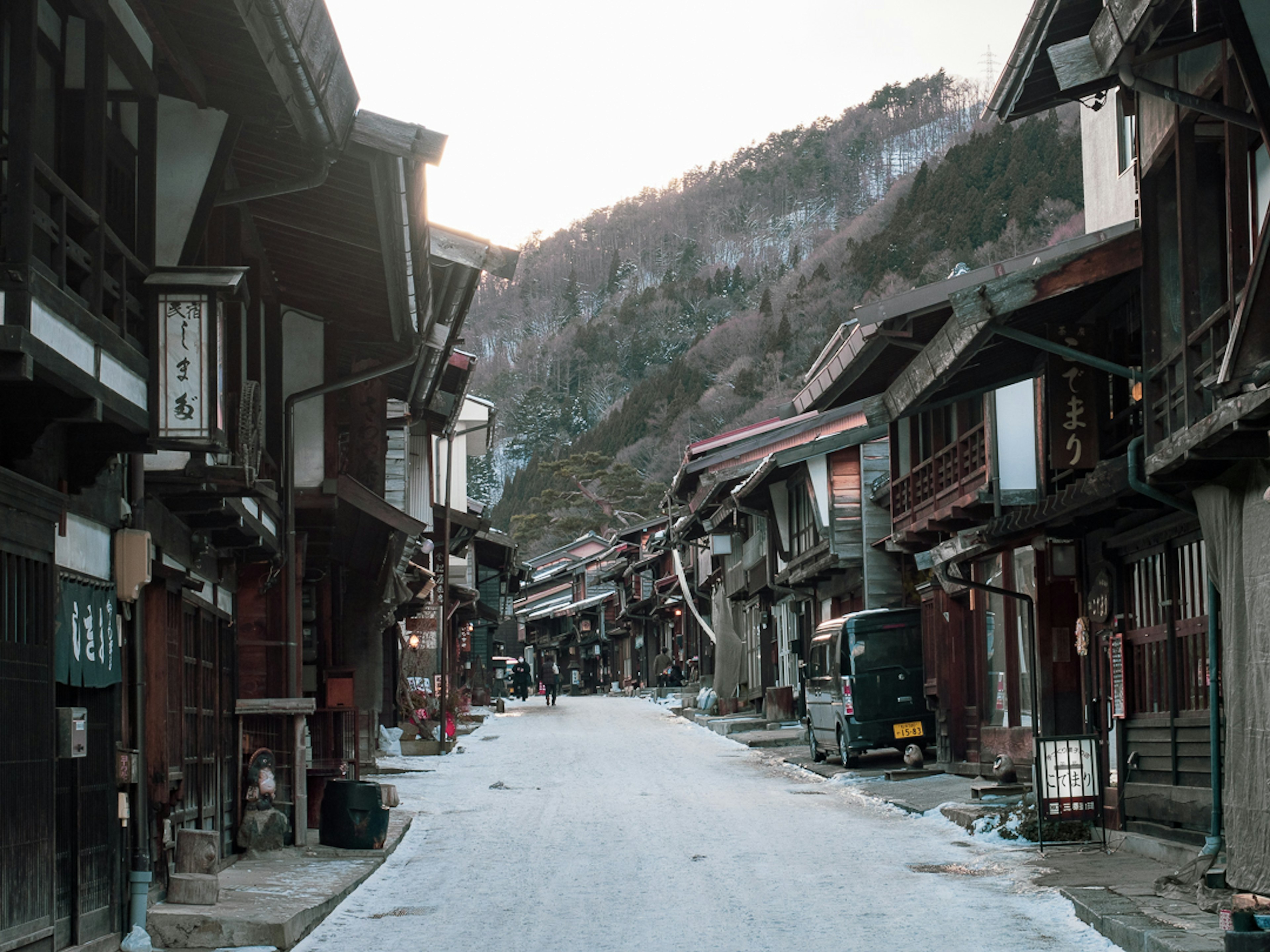 Snow-covered traditional street with wooden buildings and mountains