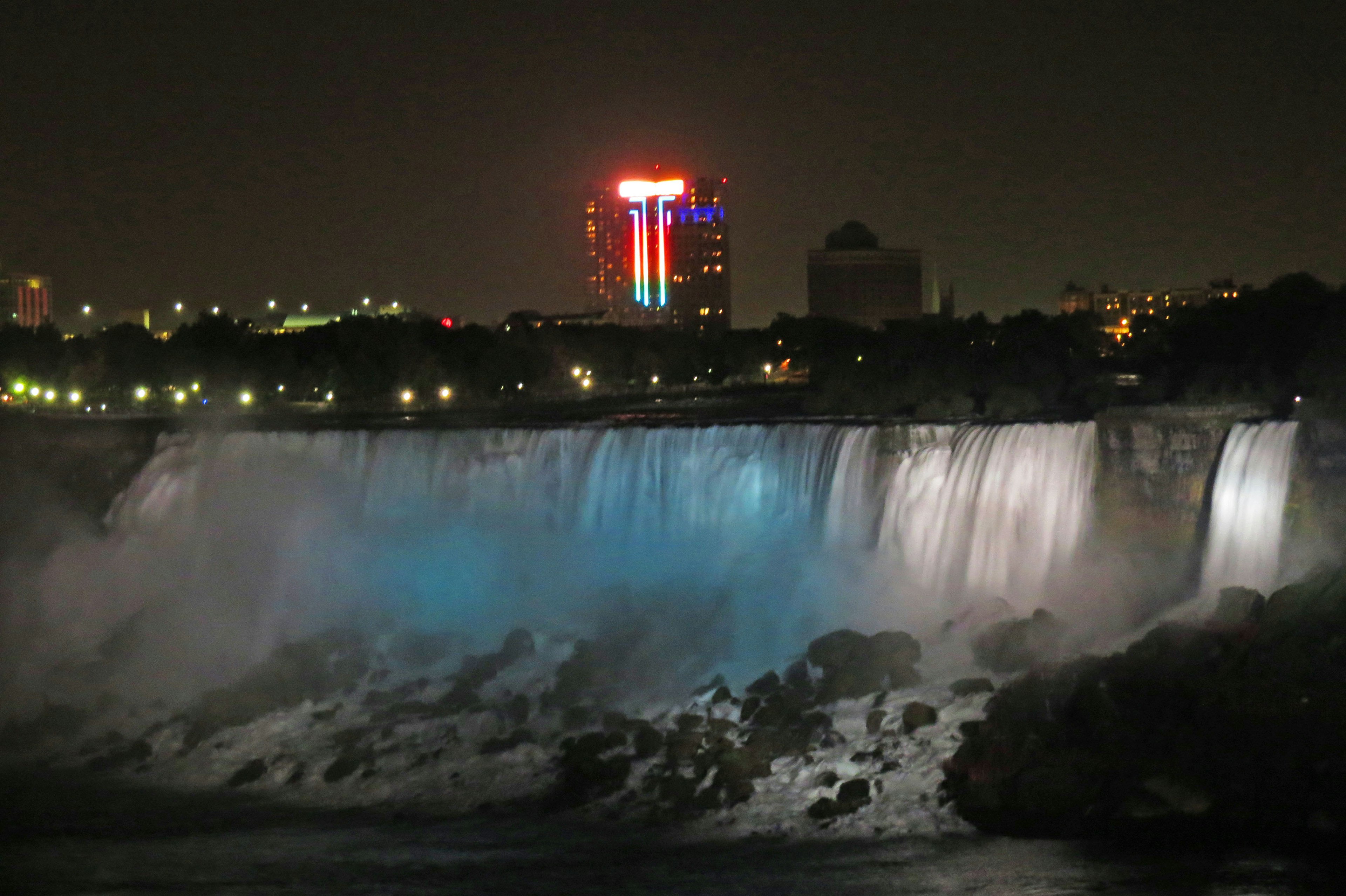 Vue nocturne des chutes du Niagara illuminées par des lumières bleues et des bâtiments environnants