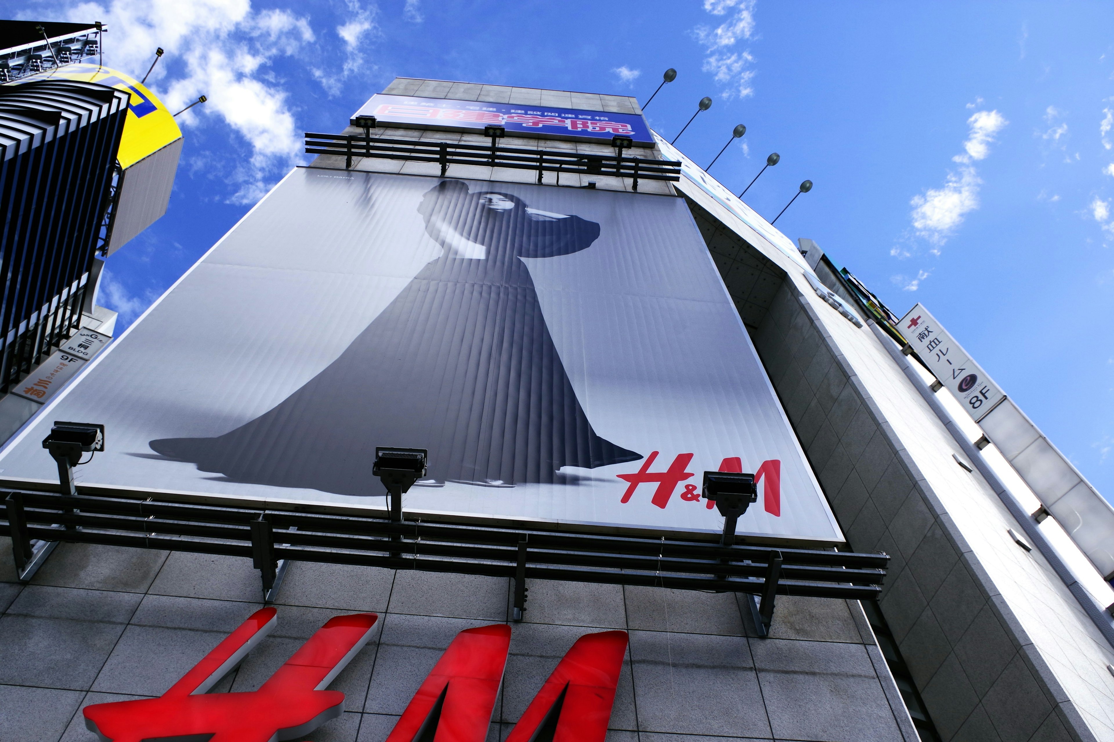 Cartellone pubblicitario H&M con la silhouette di un vestito nero sotto un cielo blu