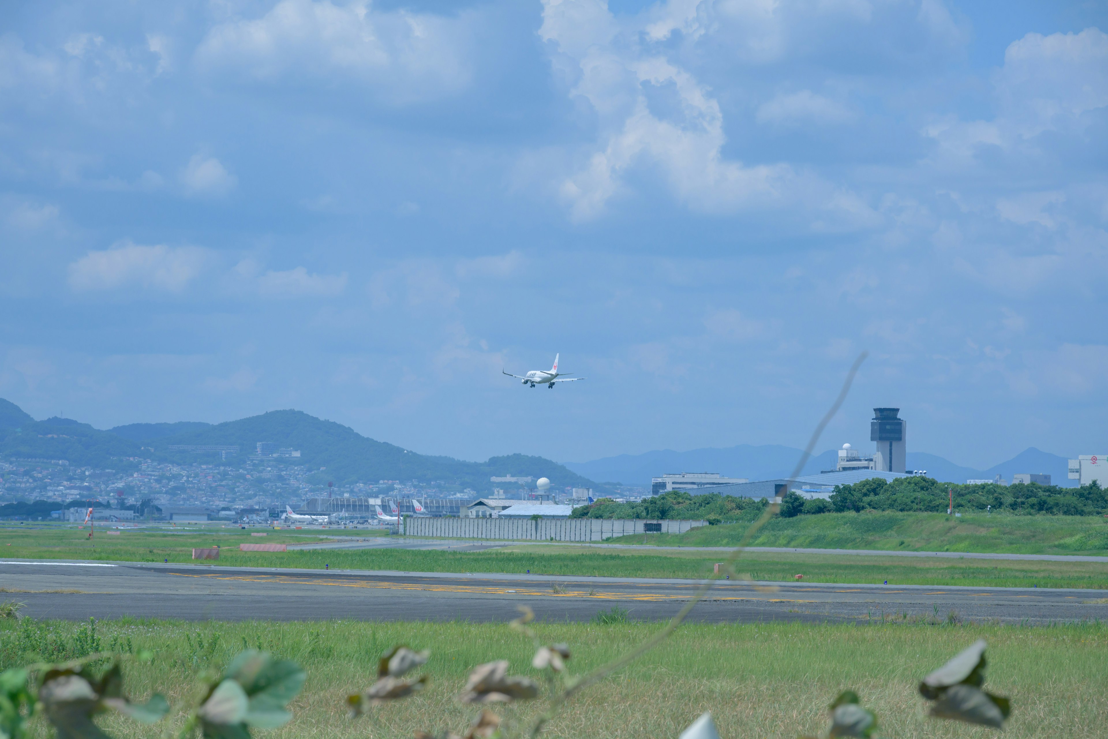 Ein Flugzeug fliegt über eine Flughafenpiste unter einem blauen Himmel