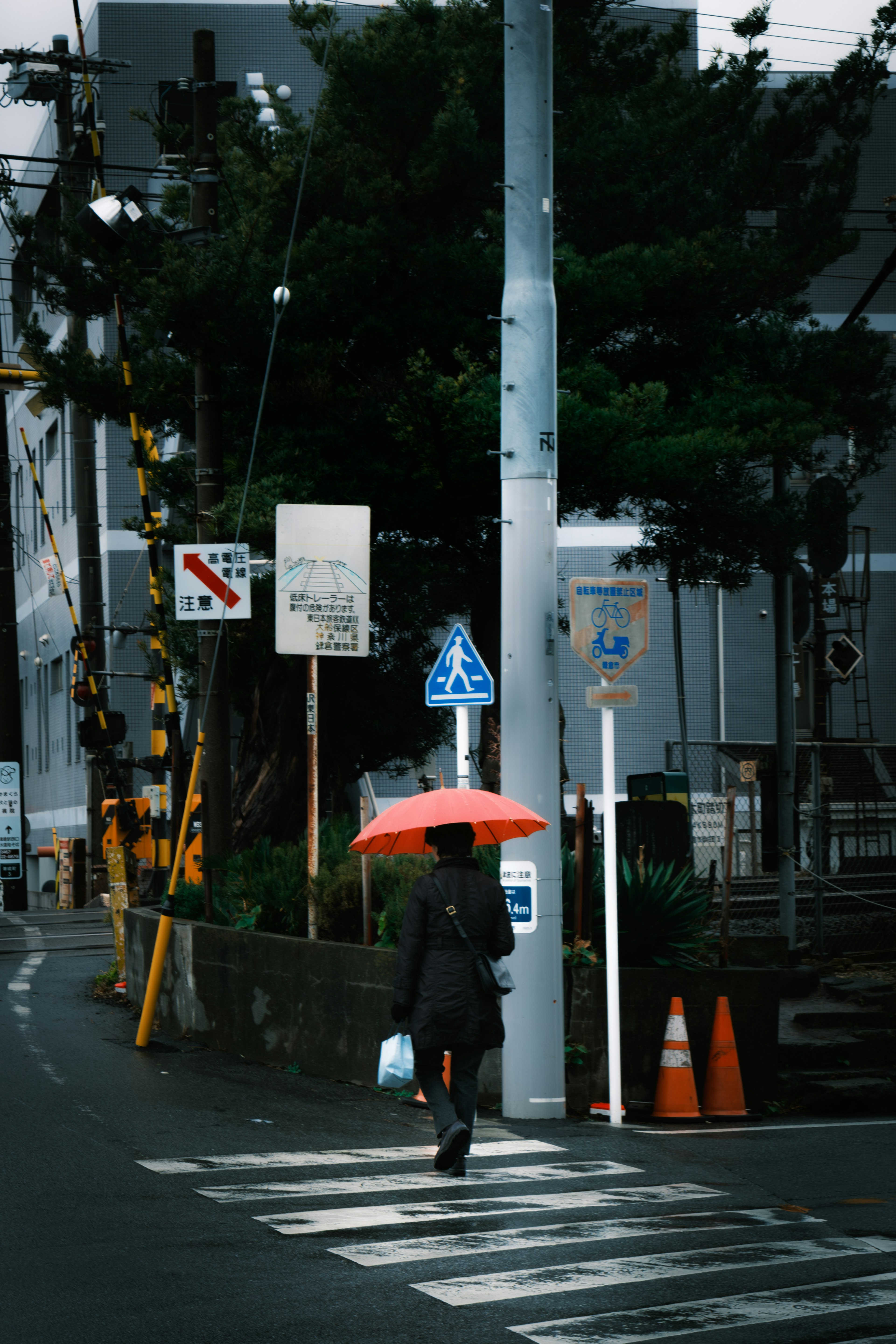 赤い傘をさした人が横断歩道を渡る都市の風景