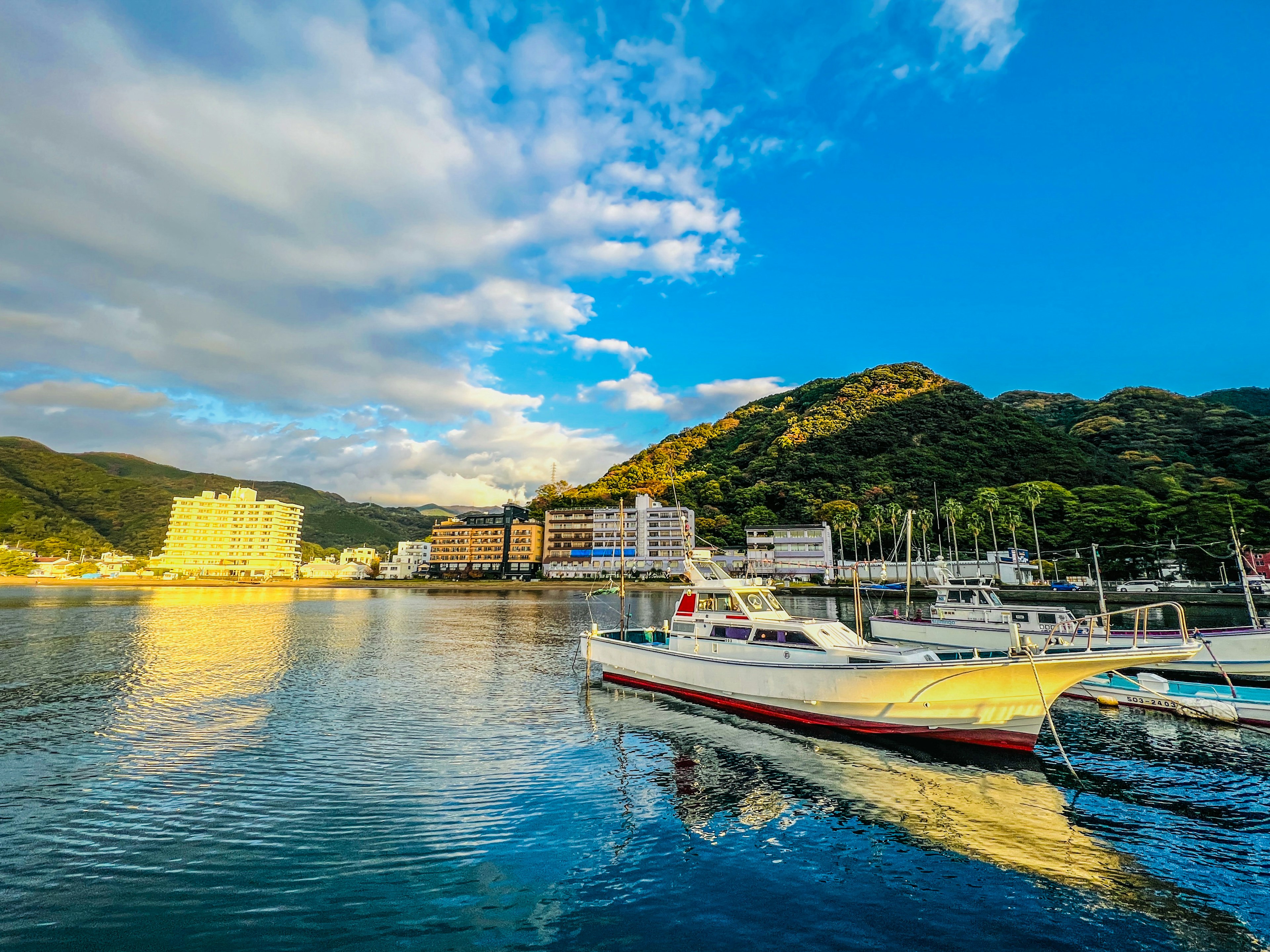 Vista panoramica di una barca bianca su acqua calma con montagne e edifici sullo sfondo