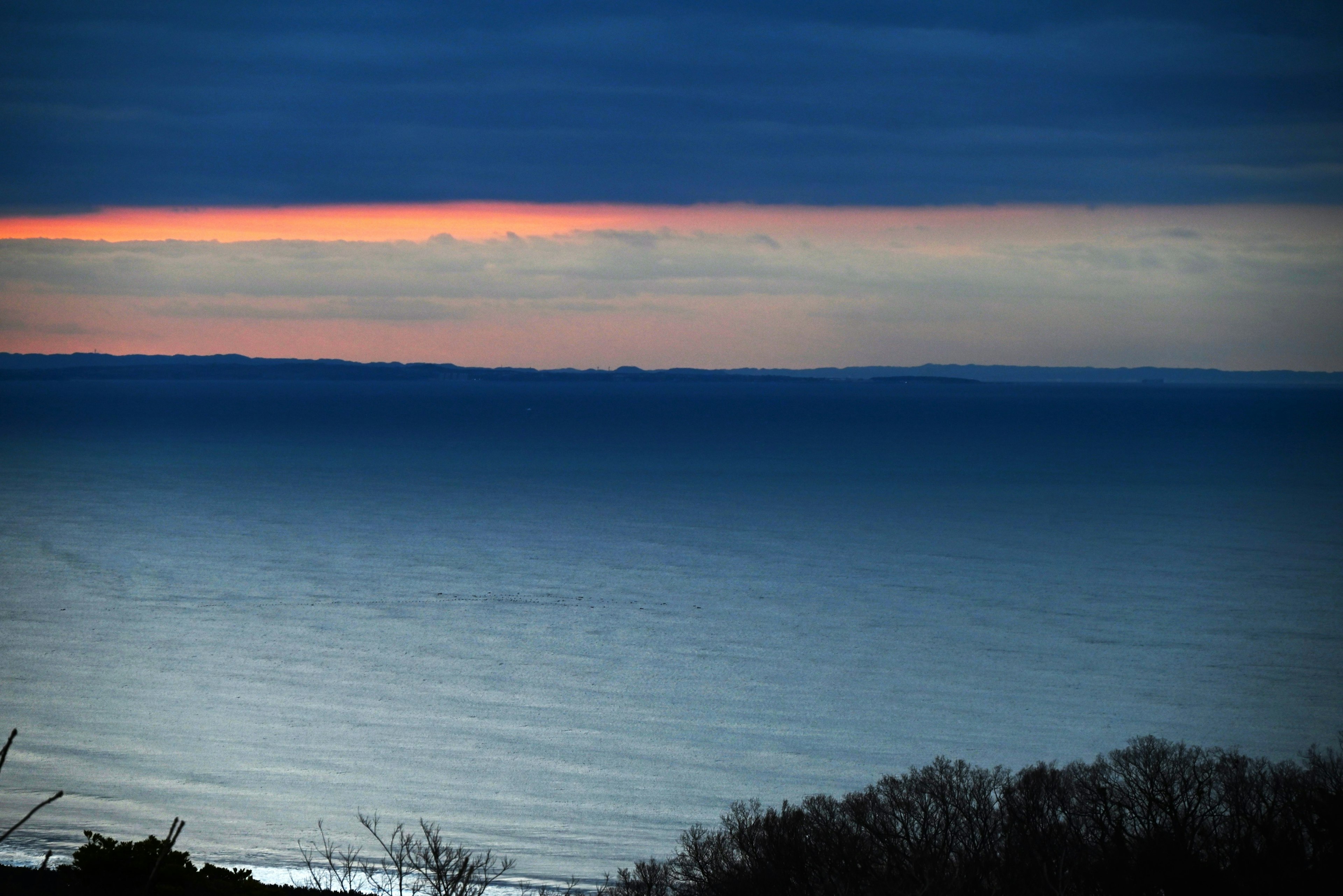 Un paysage de mer bleue et ciel sombre avec une ligne orange de coucher de soleil