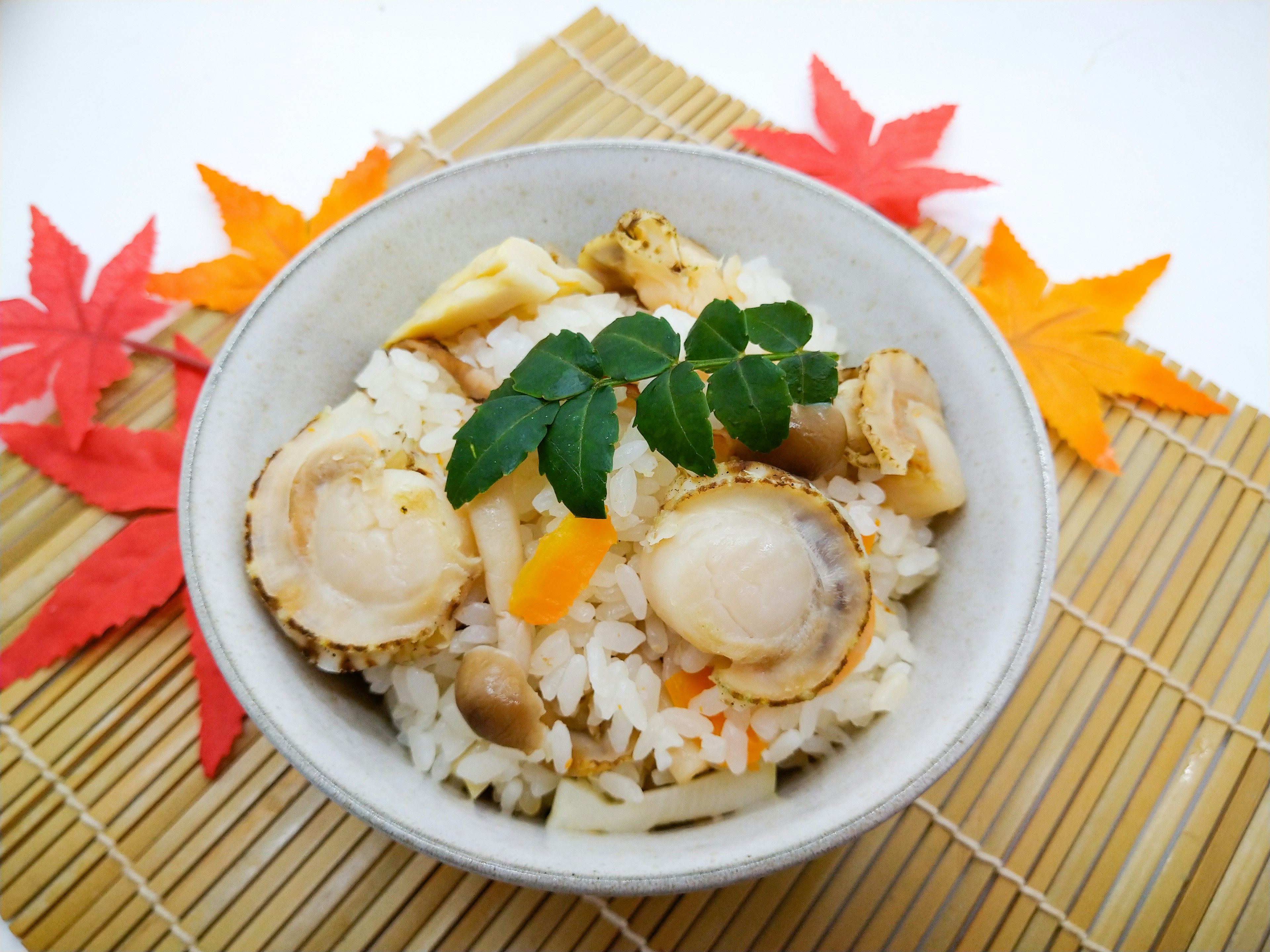 Un bol de riz garni de coquillages et de légumes entouré de feuilles d'automne