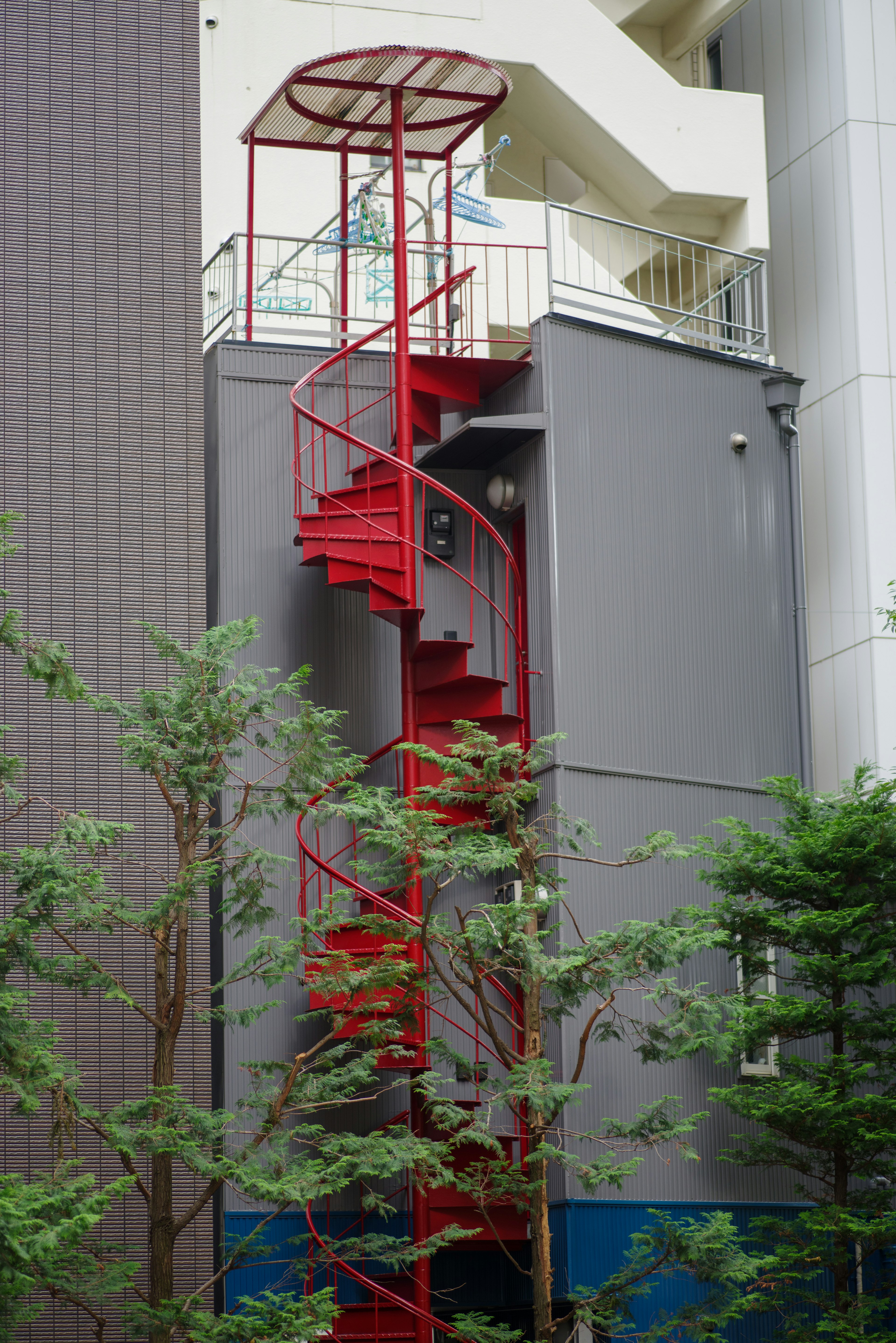 Außenansicht eines Gebäudes mit einer roten Wendeltreppe umgeben von grünen Bäumen