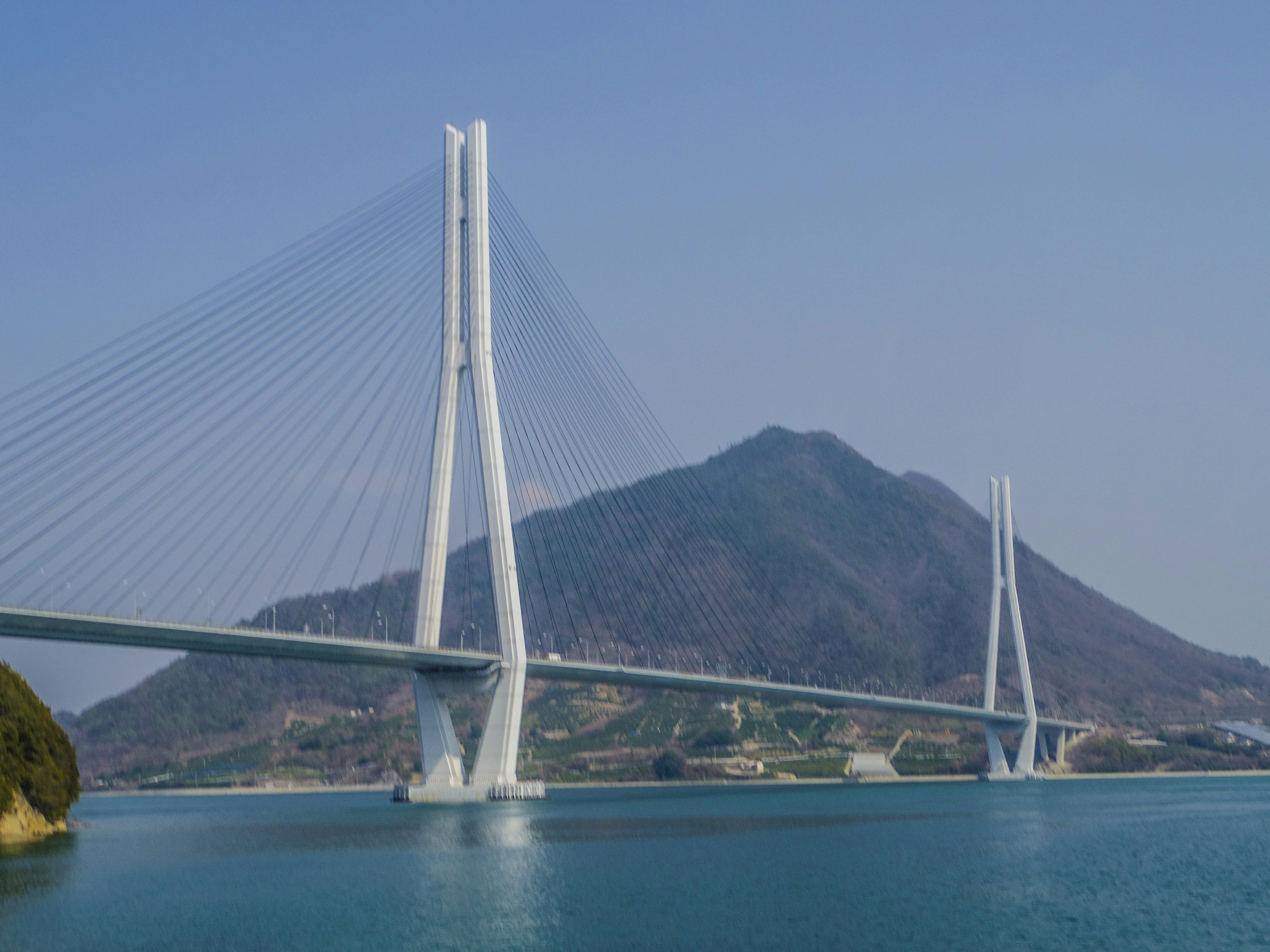 Weißer Hängebrücke vor blauem Himmel und Berg