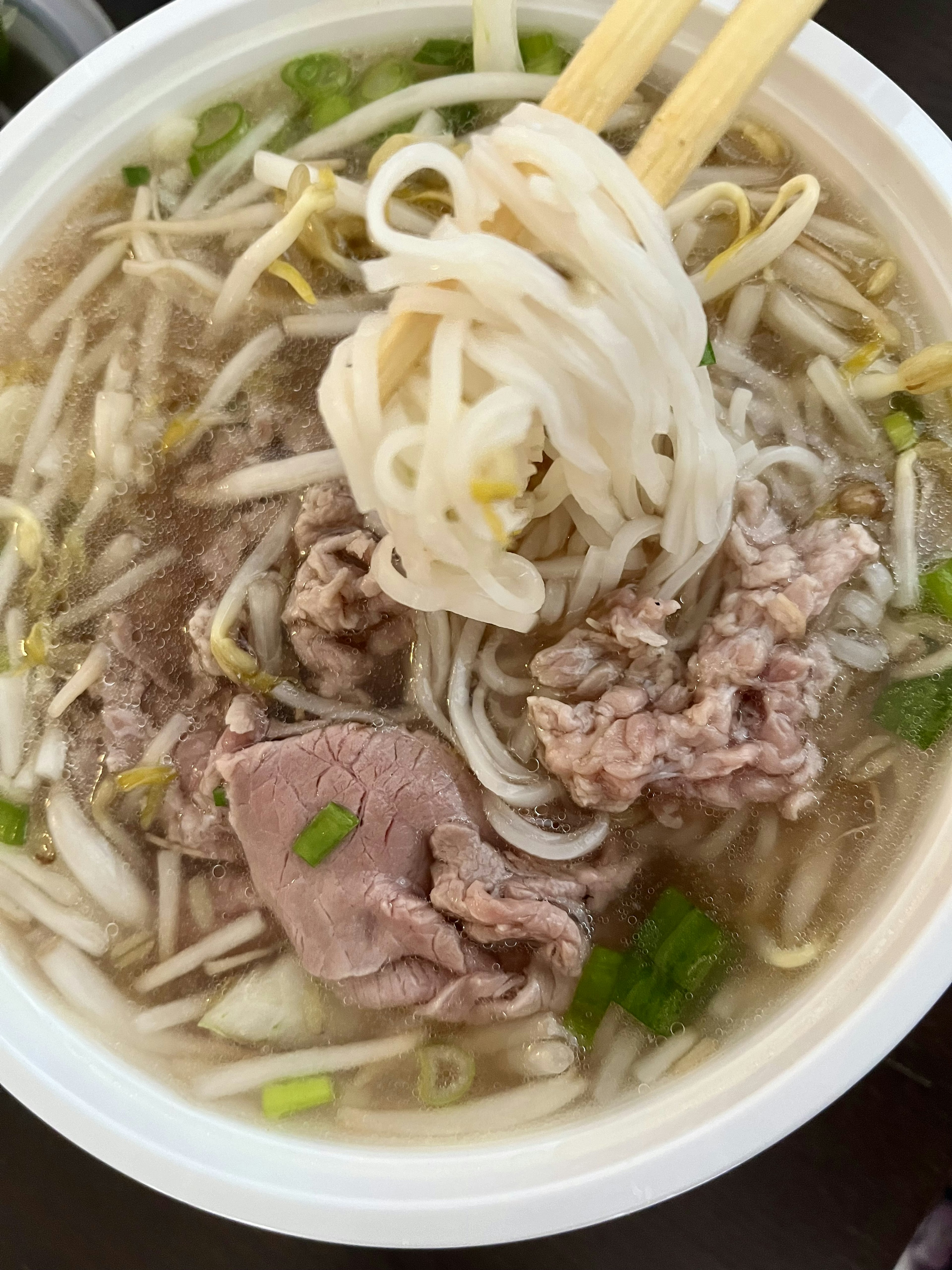 A bowl of clear soup with rice noodles and slices of beef