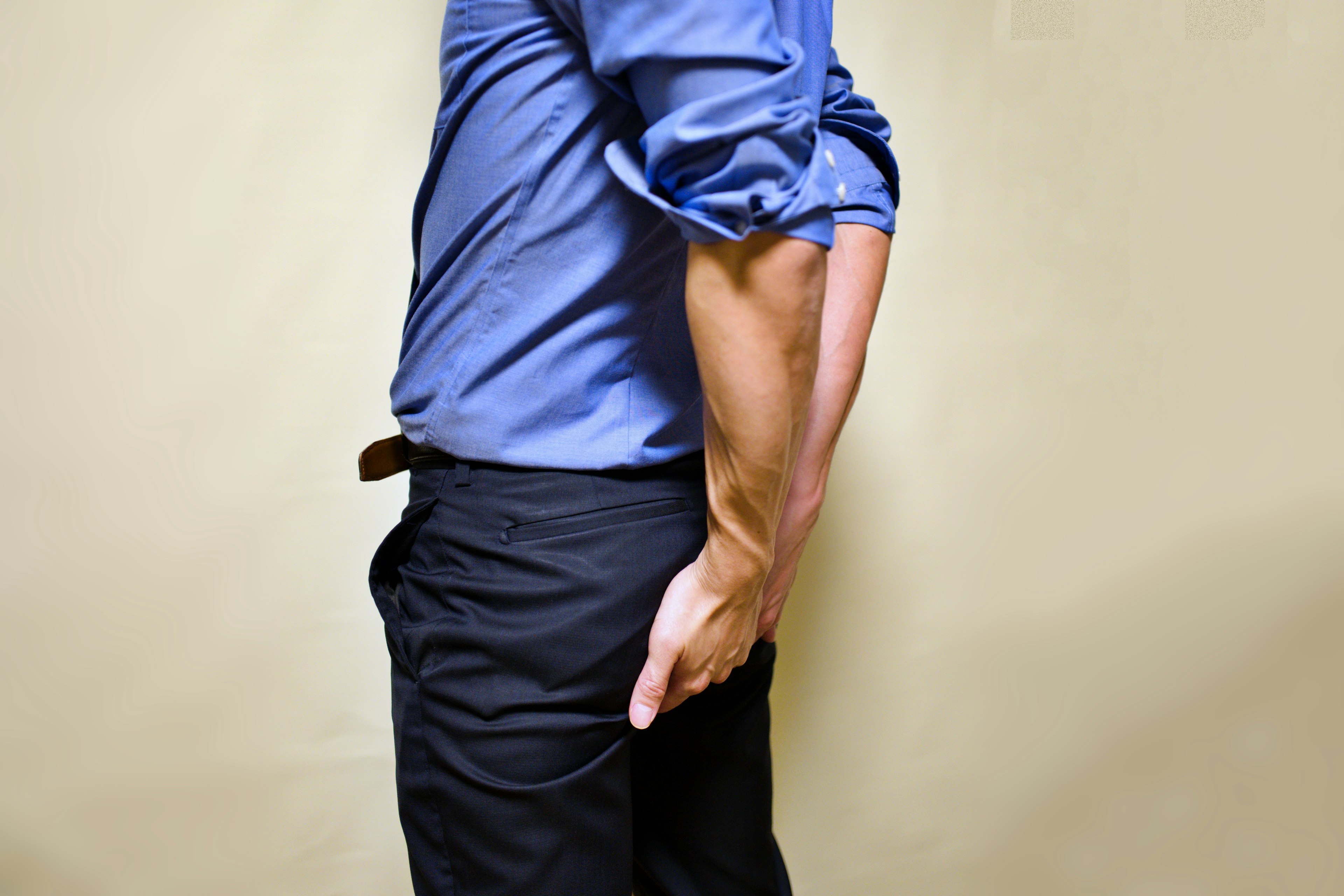 Man in blue shirt standing sideways with hands clasped behind his back