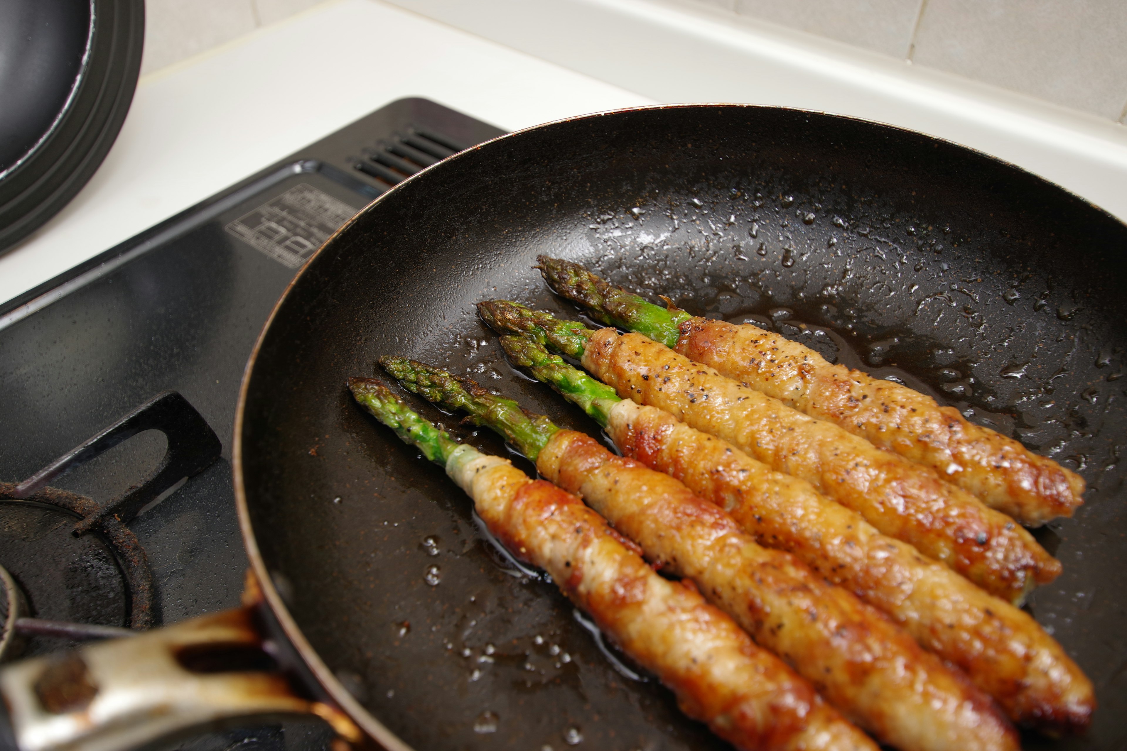 Asparagus wrapped in bacon cooking in a frying pan