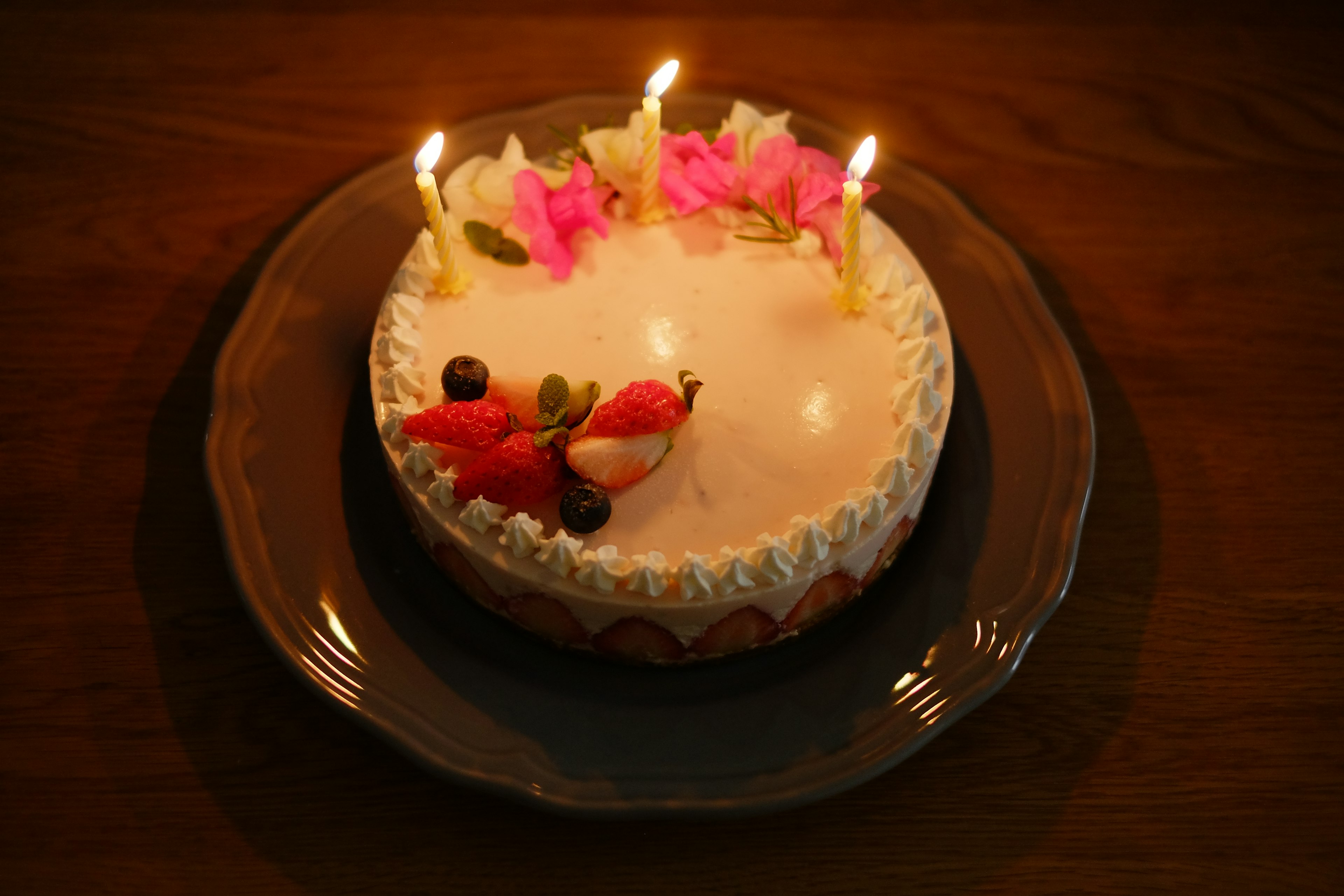 Cream cake decorated with flowers and fruits topped with three lit candles