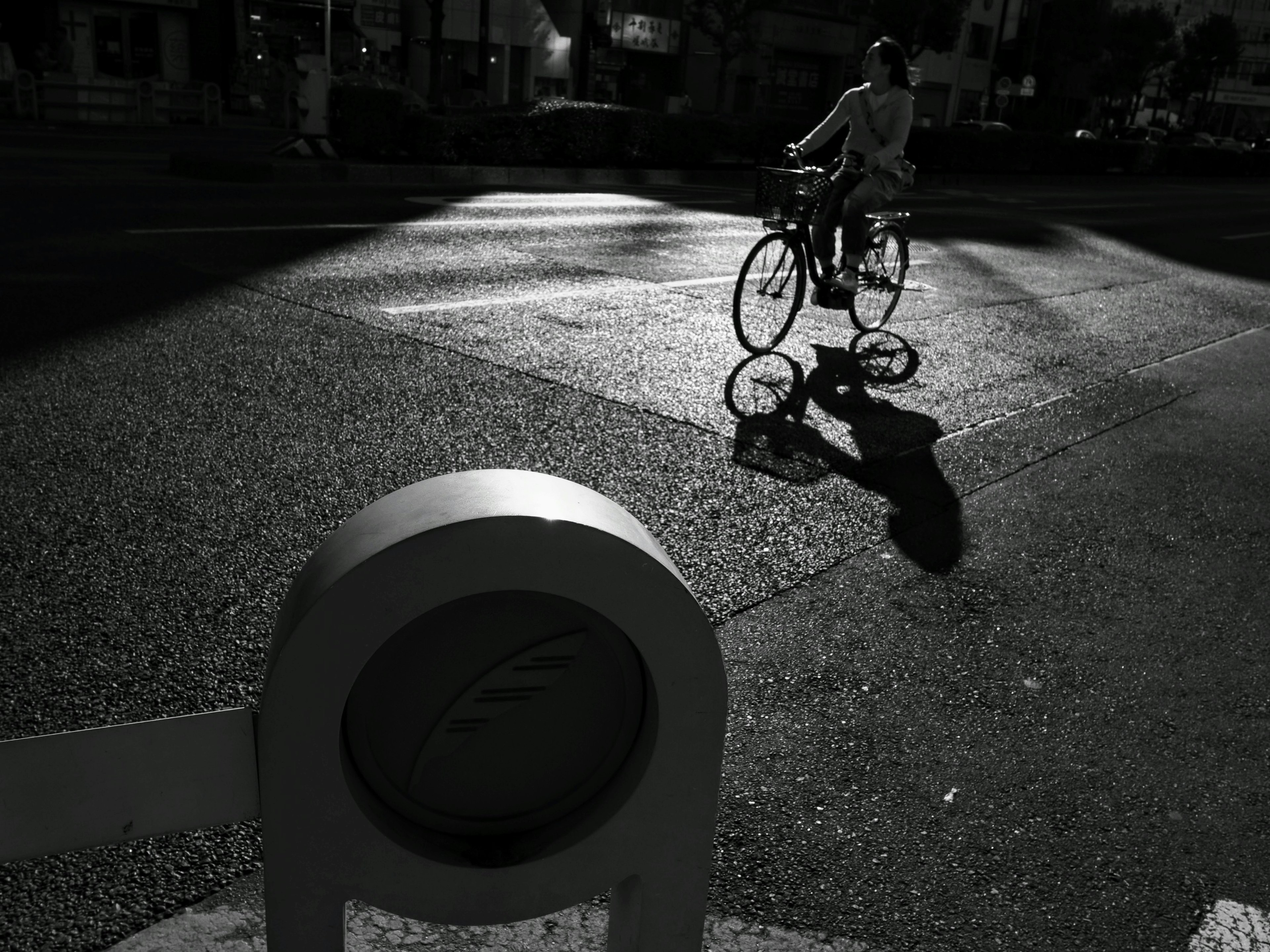 Un cycliste traversant une intersection projetant des ombres dans une scène en noir et blanc