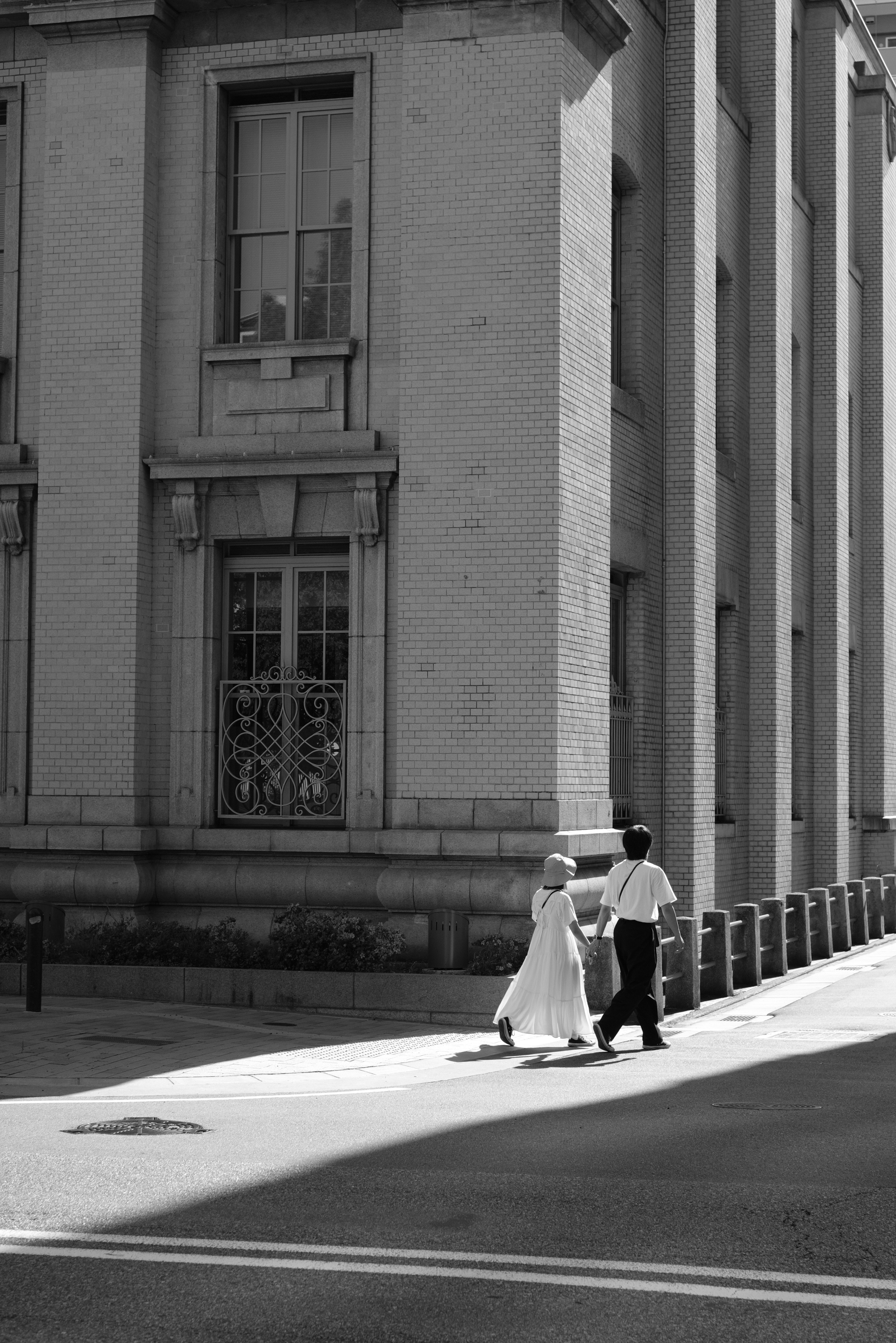 Photo en noir et blanc d'une femme en robe blanche et d'un homme en costume marchant à un coin de rue