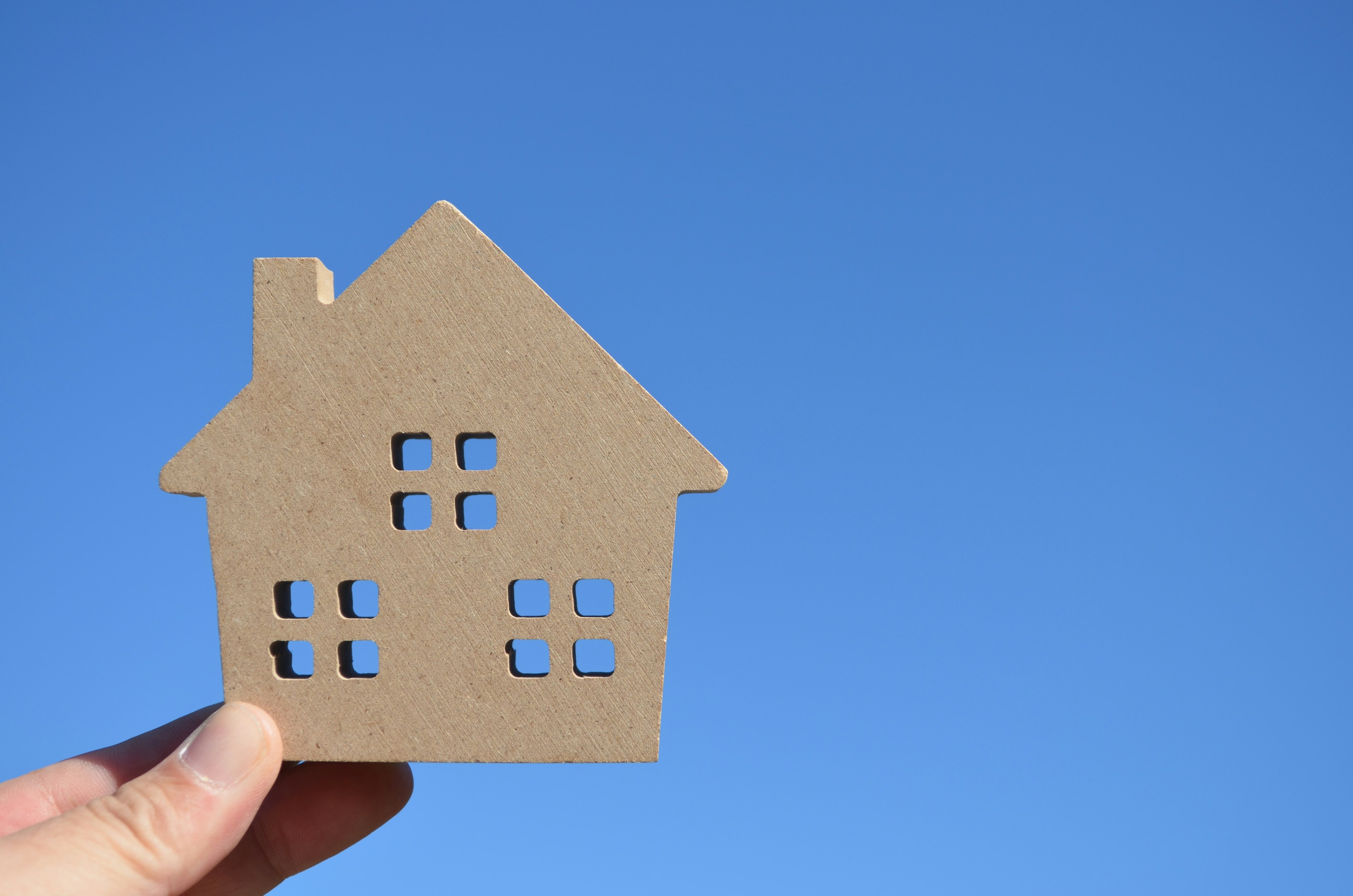 Une main tenant une forme de maison en carton brun contre un ciel bleu