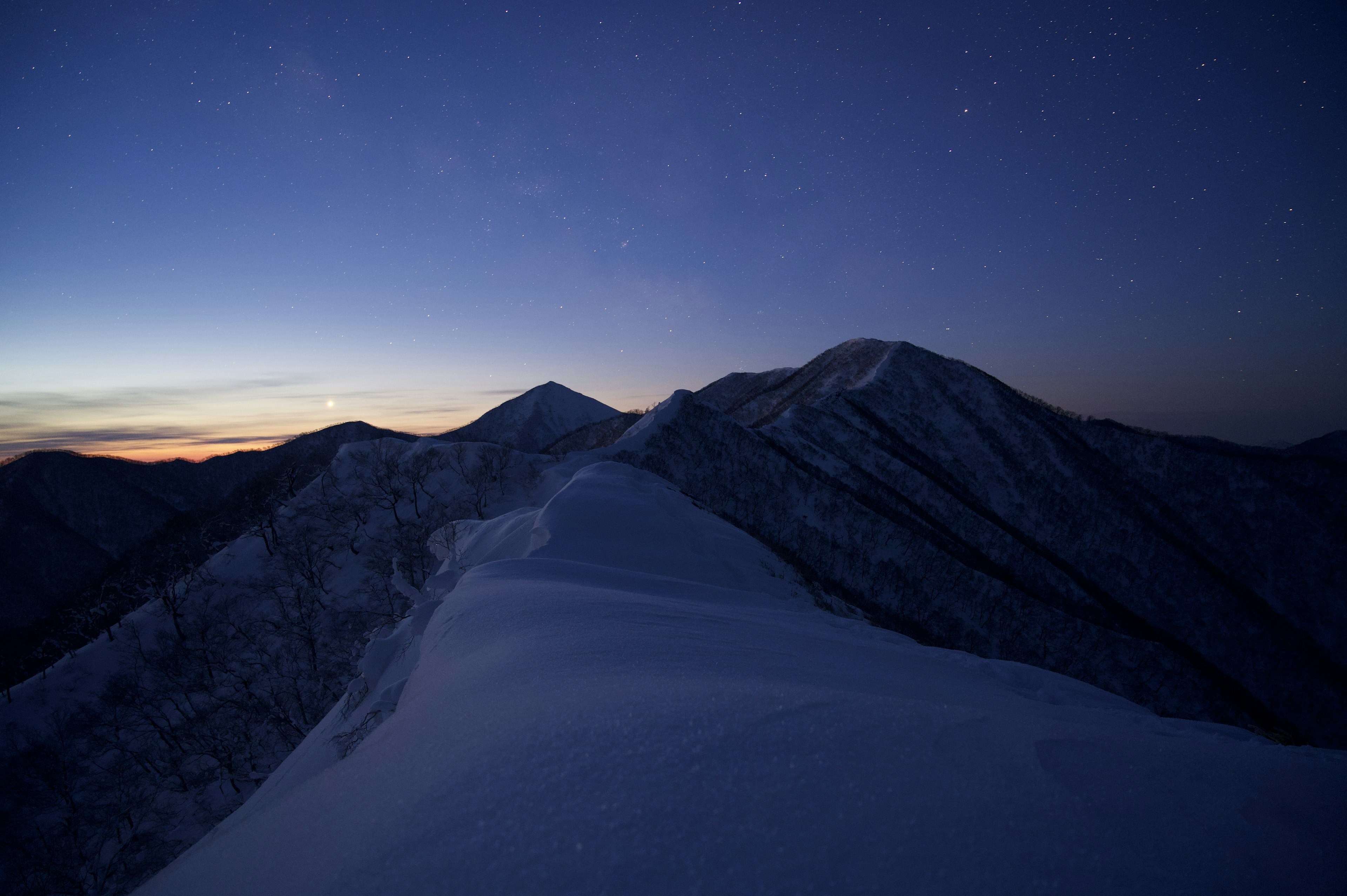 雪に覆われた山々と星空が広がる夕暮れの風景