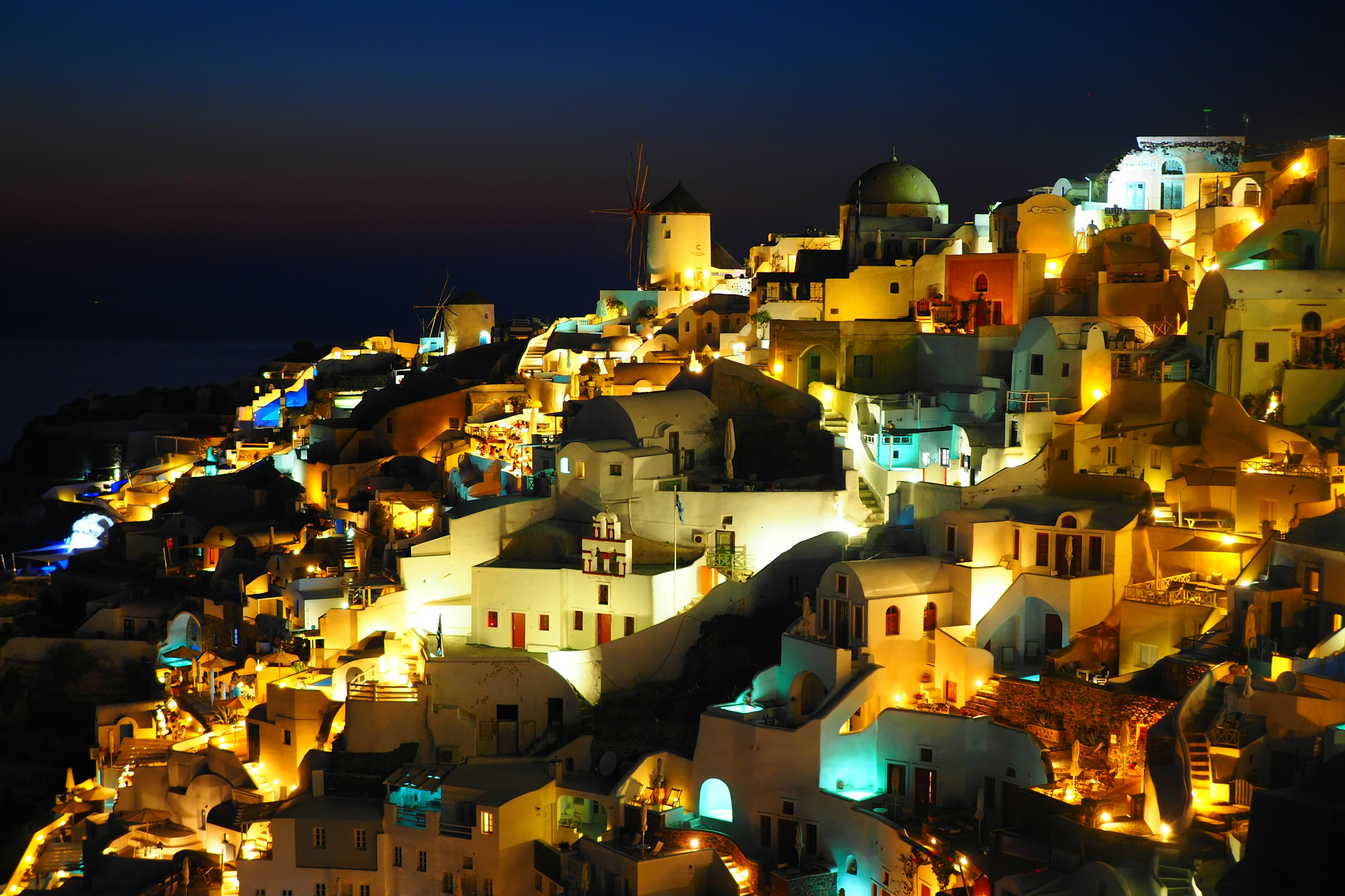 Splendida vista notturna di Santorini con case bianche illuminate da luci arancioni