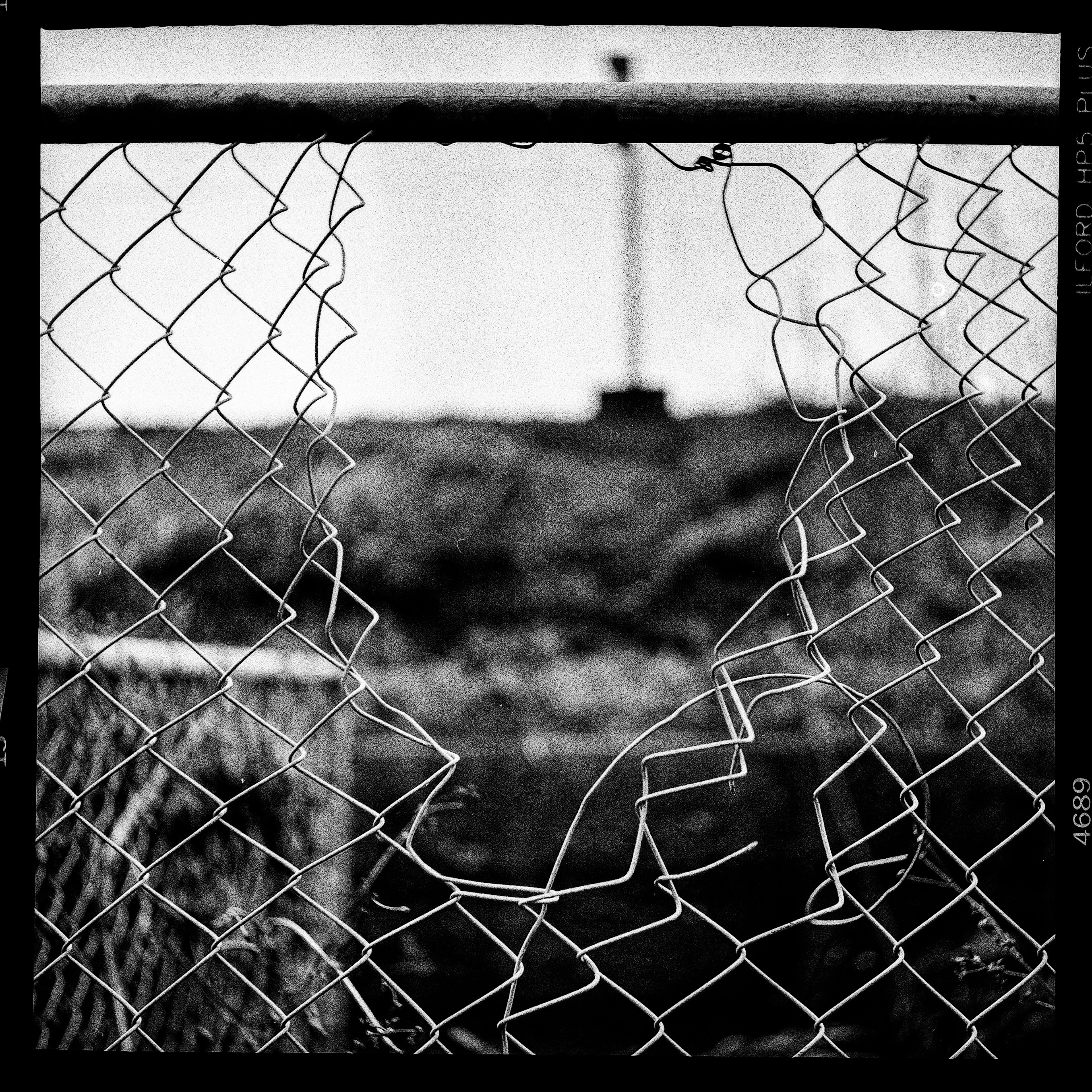 Photo en noir et blanc d'une clôture en fil de fer barbelé déchirée avec un paysage flou en arrière-plan