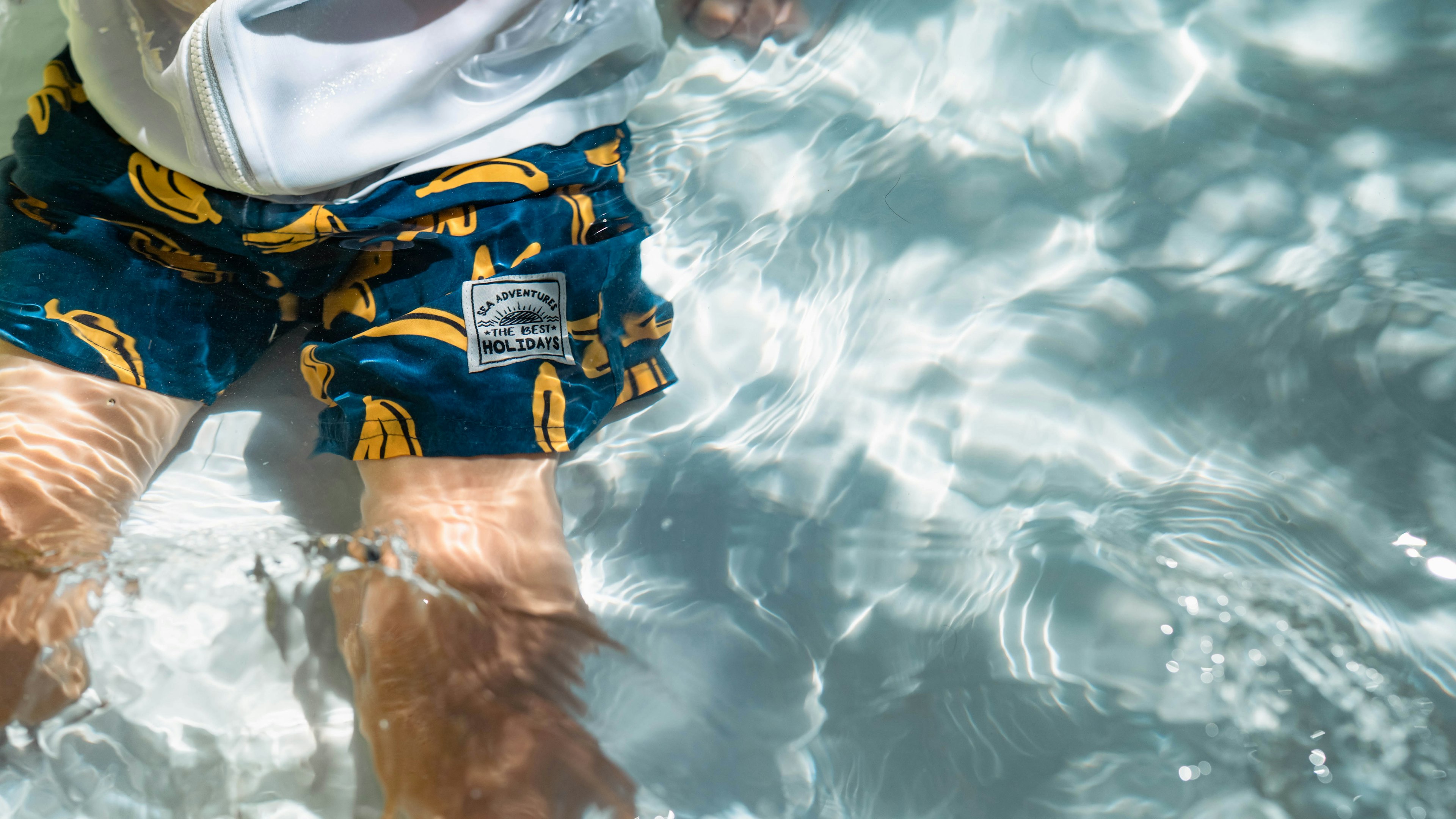 Person's legs in water wearing banana pattern swim shorts