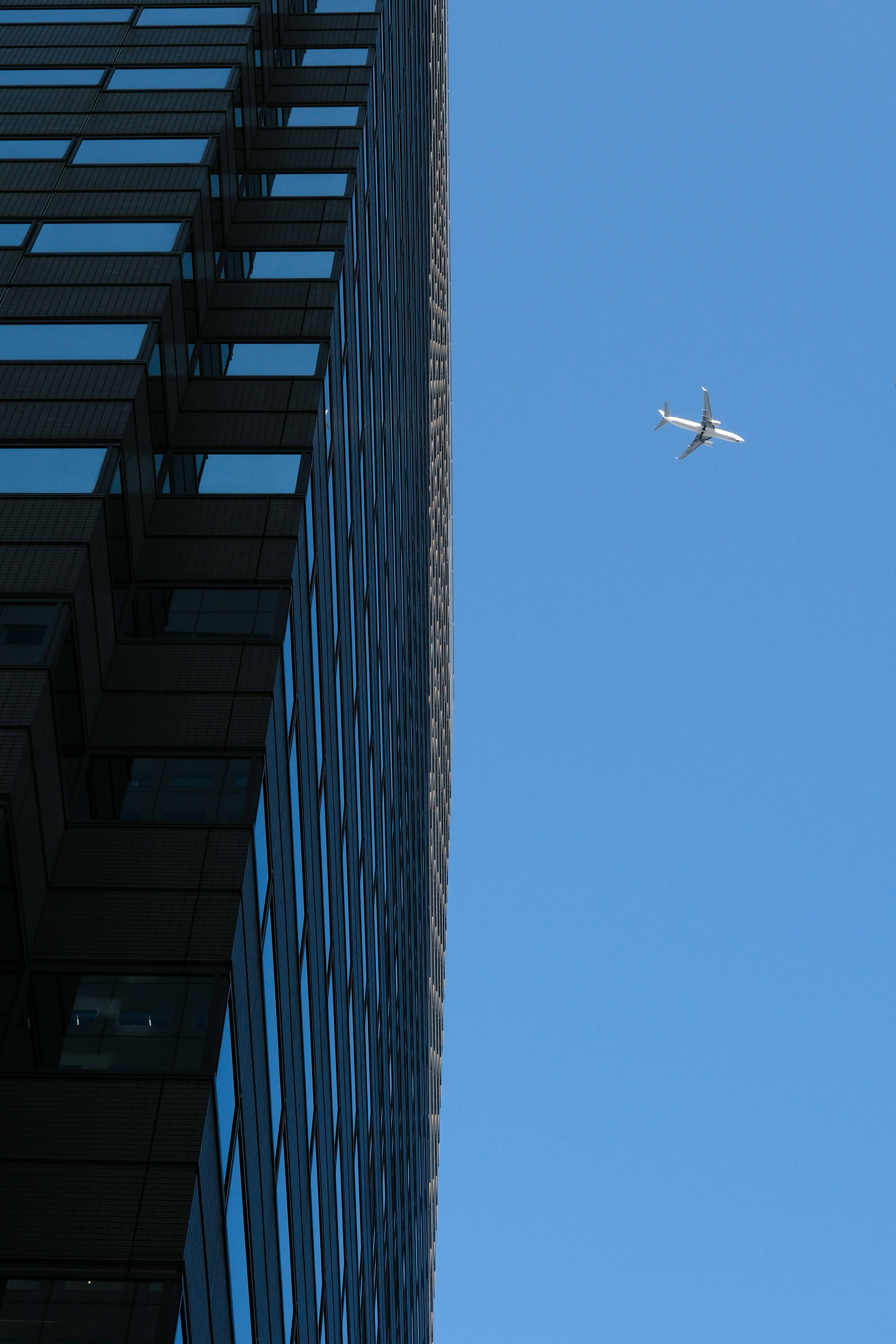 青空に飛行機と高層ビルの一部が写る