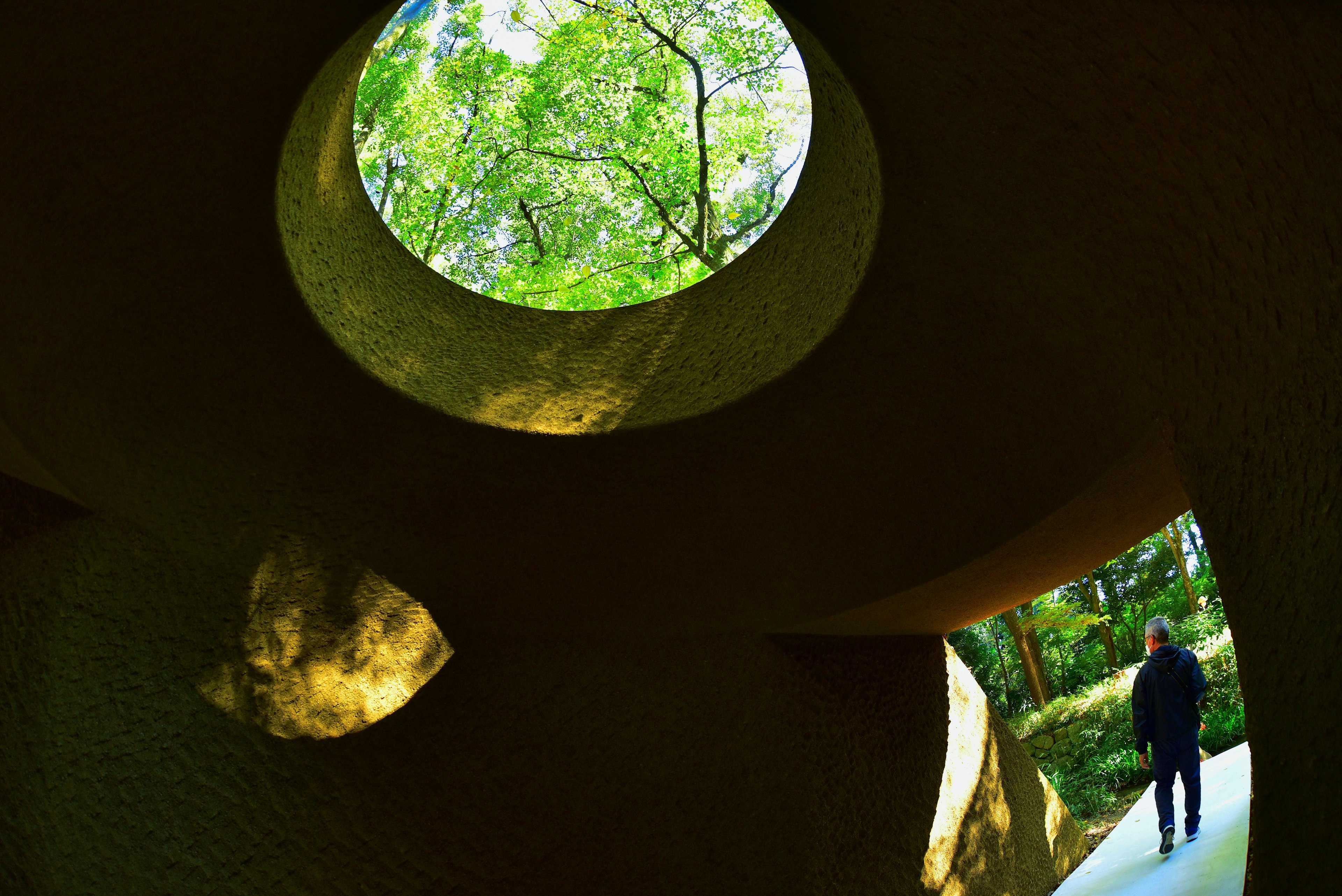 Person standing inside a sculpture with circular openings showing green trees