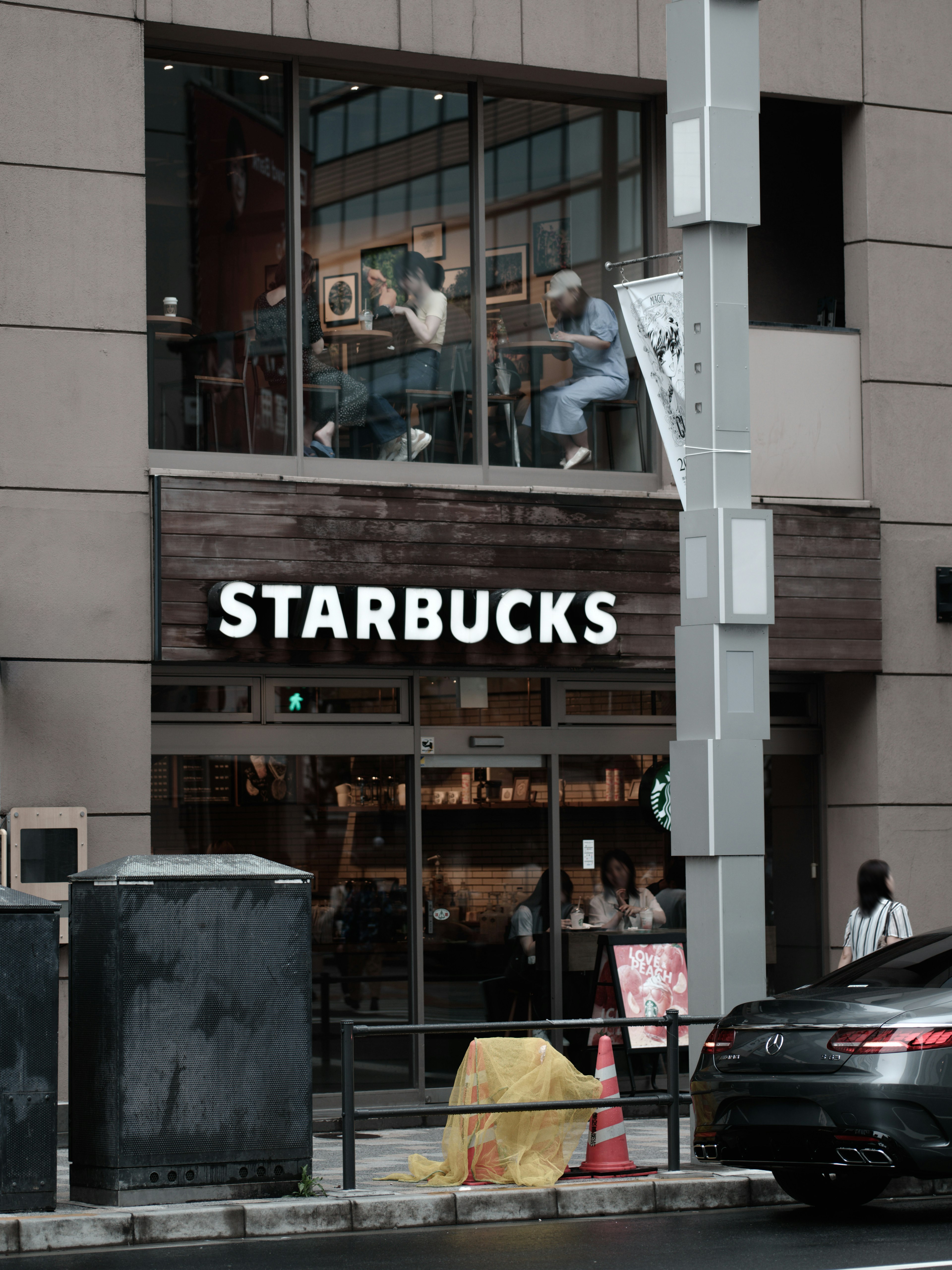 Cảnh bên ngoài cửa hàng Starbucks với khách hàng nhìn thấy bên trong qua cửa sổ xung quanh là ô tô và biển báo giao thông