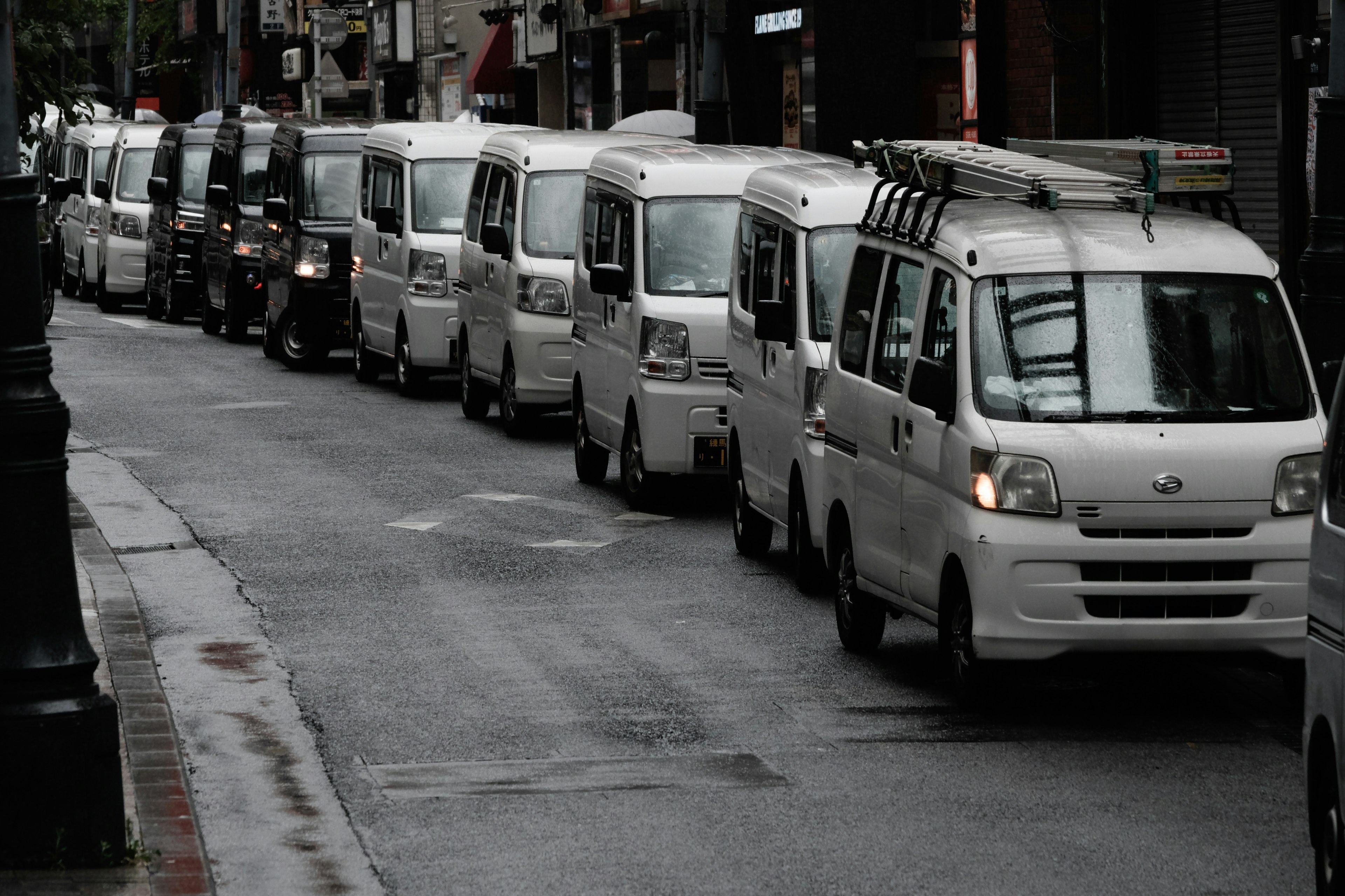 A line of white vans parked on a wet street