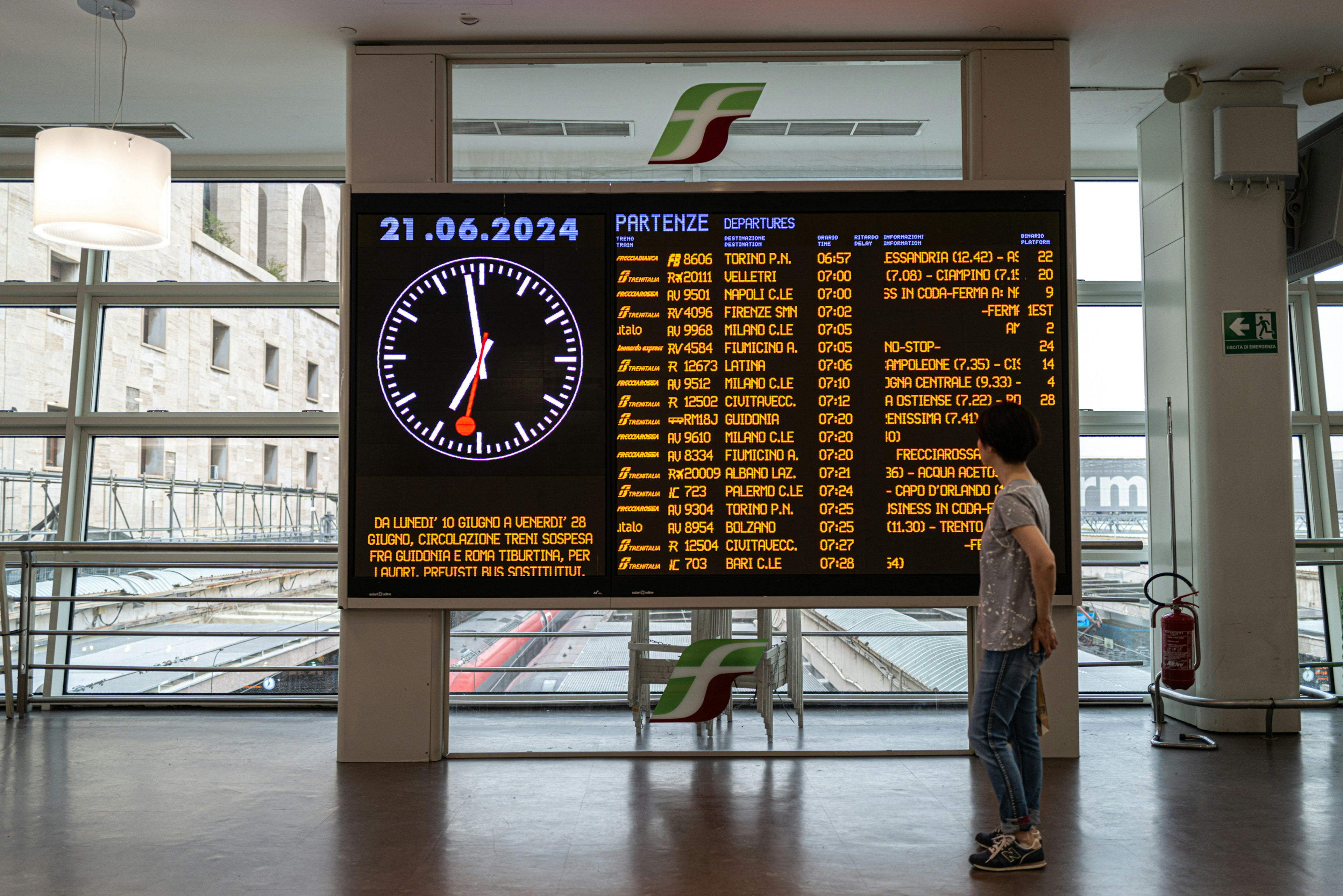 Personne devant un grand écran affichant l'horaire des trains et une horloge