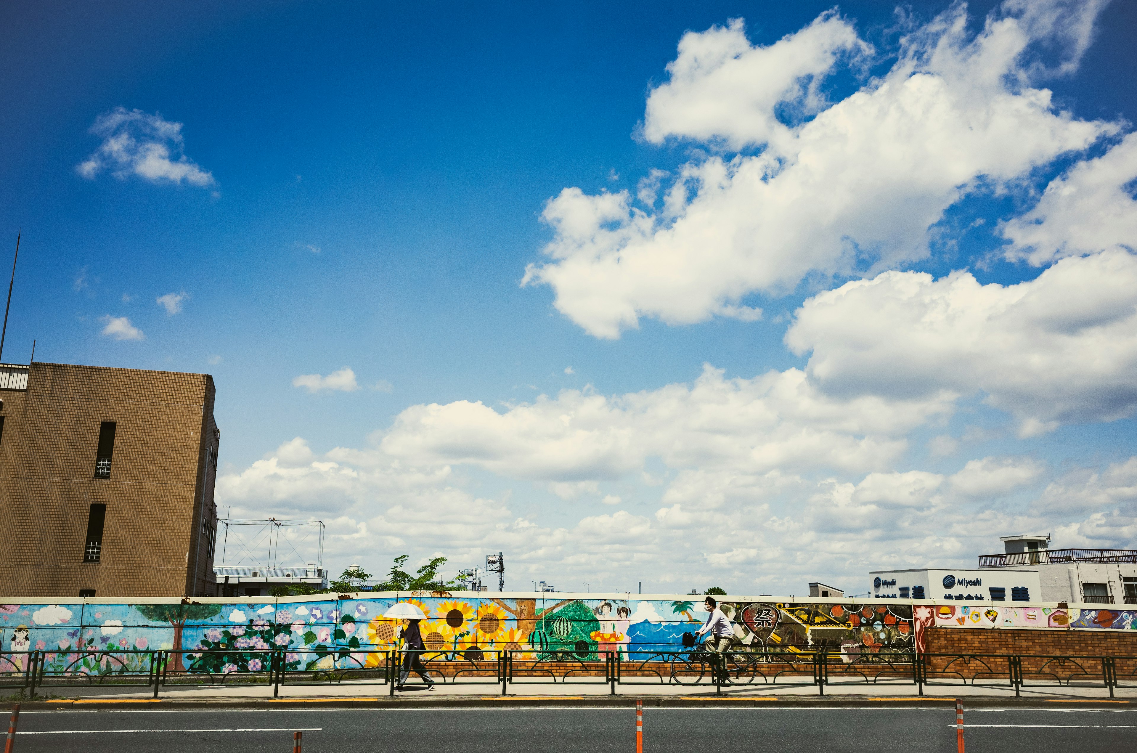 Personas caminando frente a murales coloridos bajo un cielo azul con nubes blancas