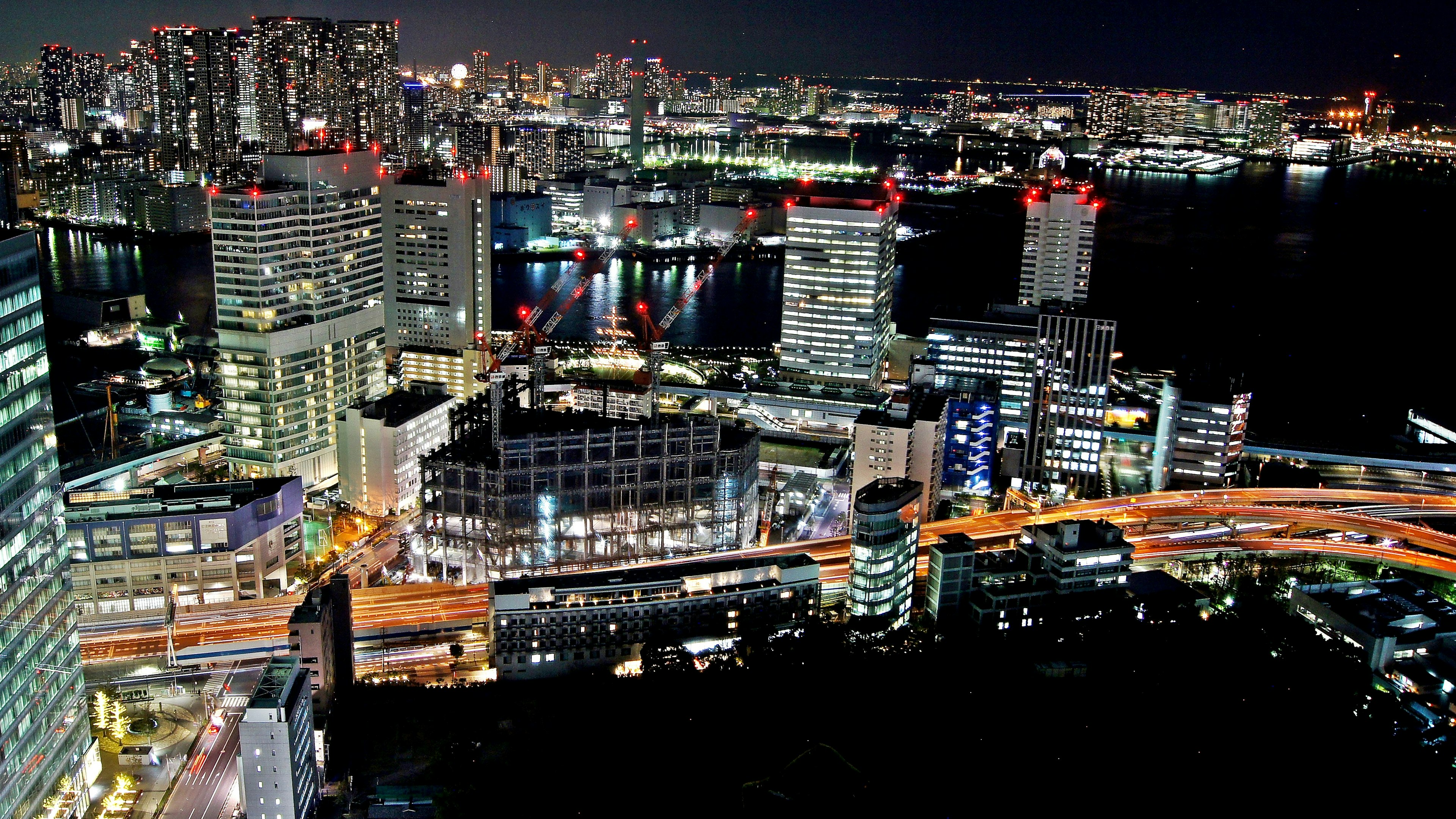 Night cityscape featuring skyscrapers and bright streetlights with traffic along the waterfront