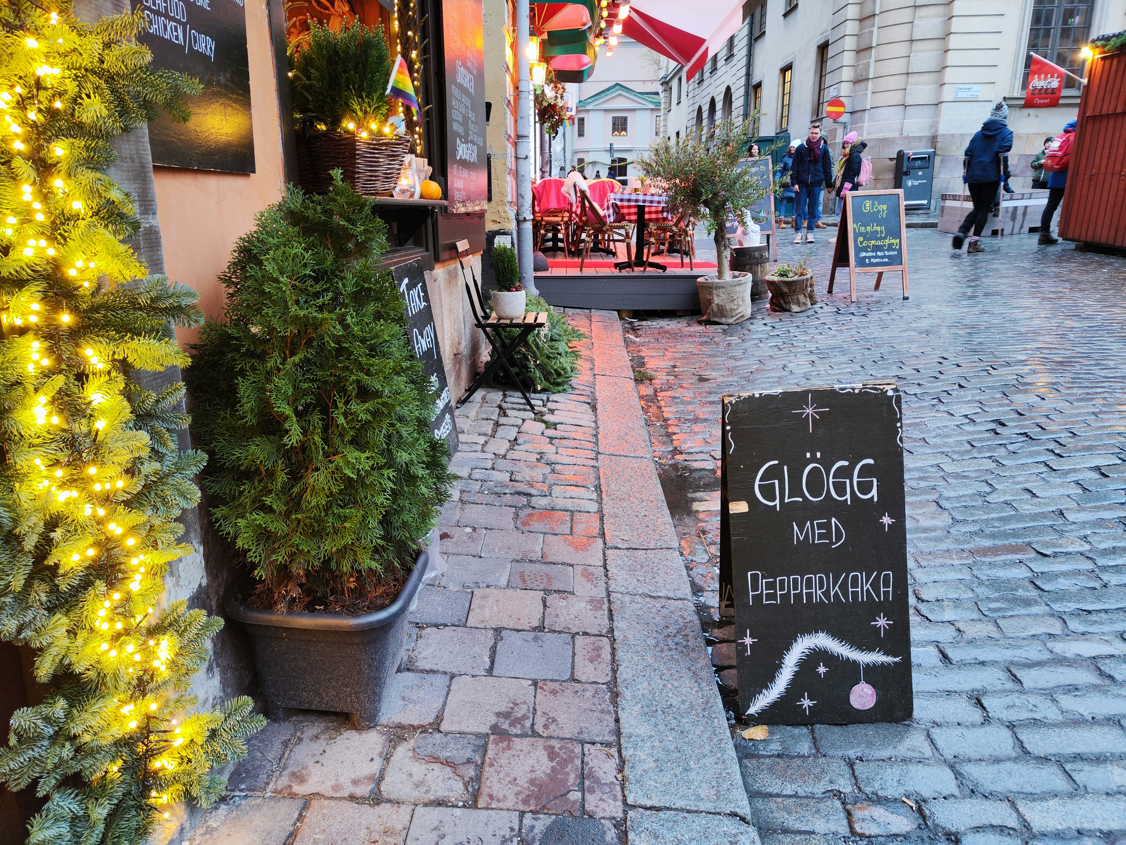 Outdoor cafe scene with a sign for glögg and pepparkaka surrounded by festive decorations