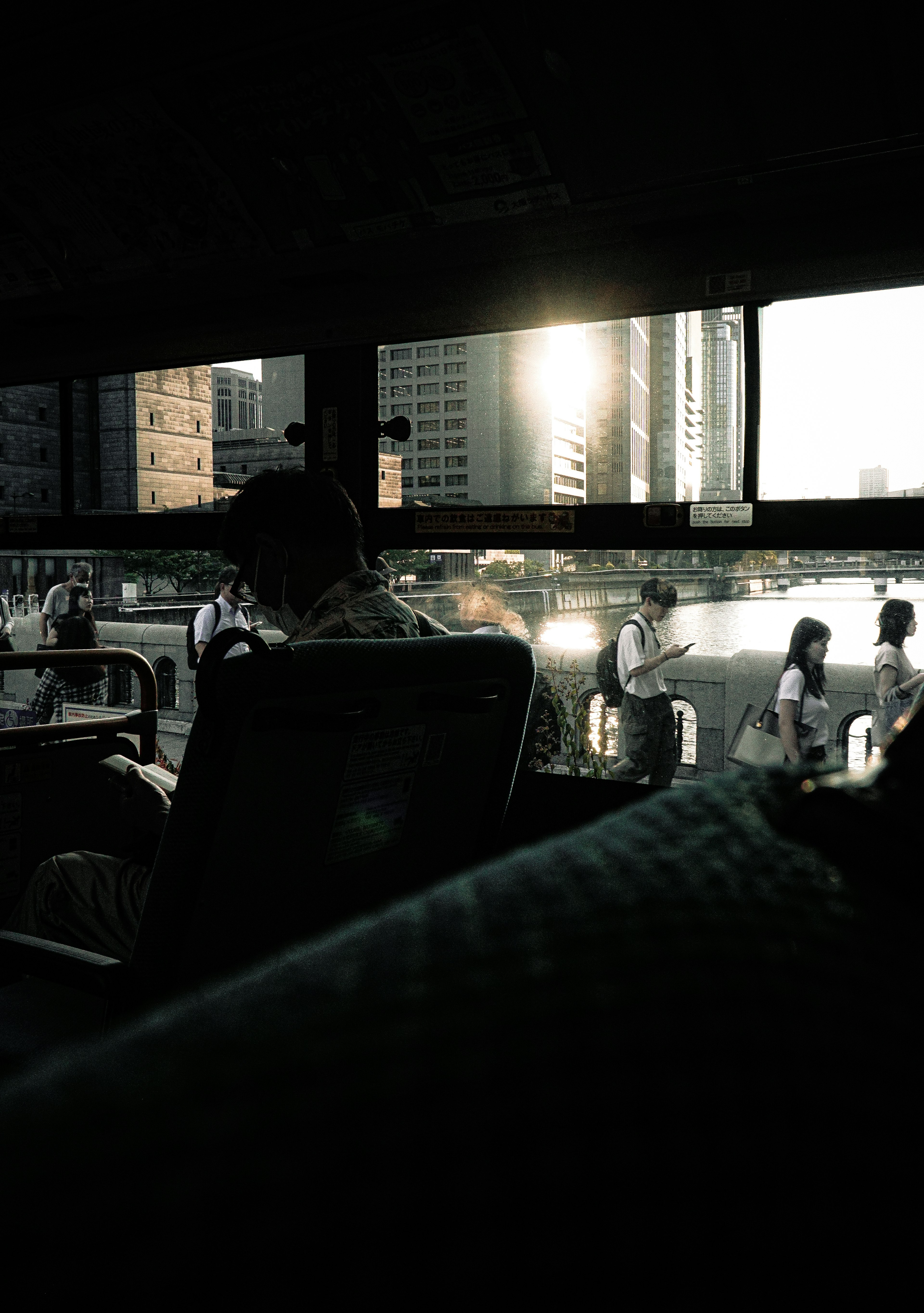 View from inside a bus with sunset lighting through buildings and passengers waiting outside