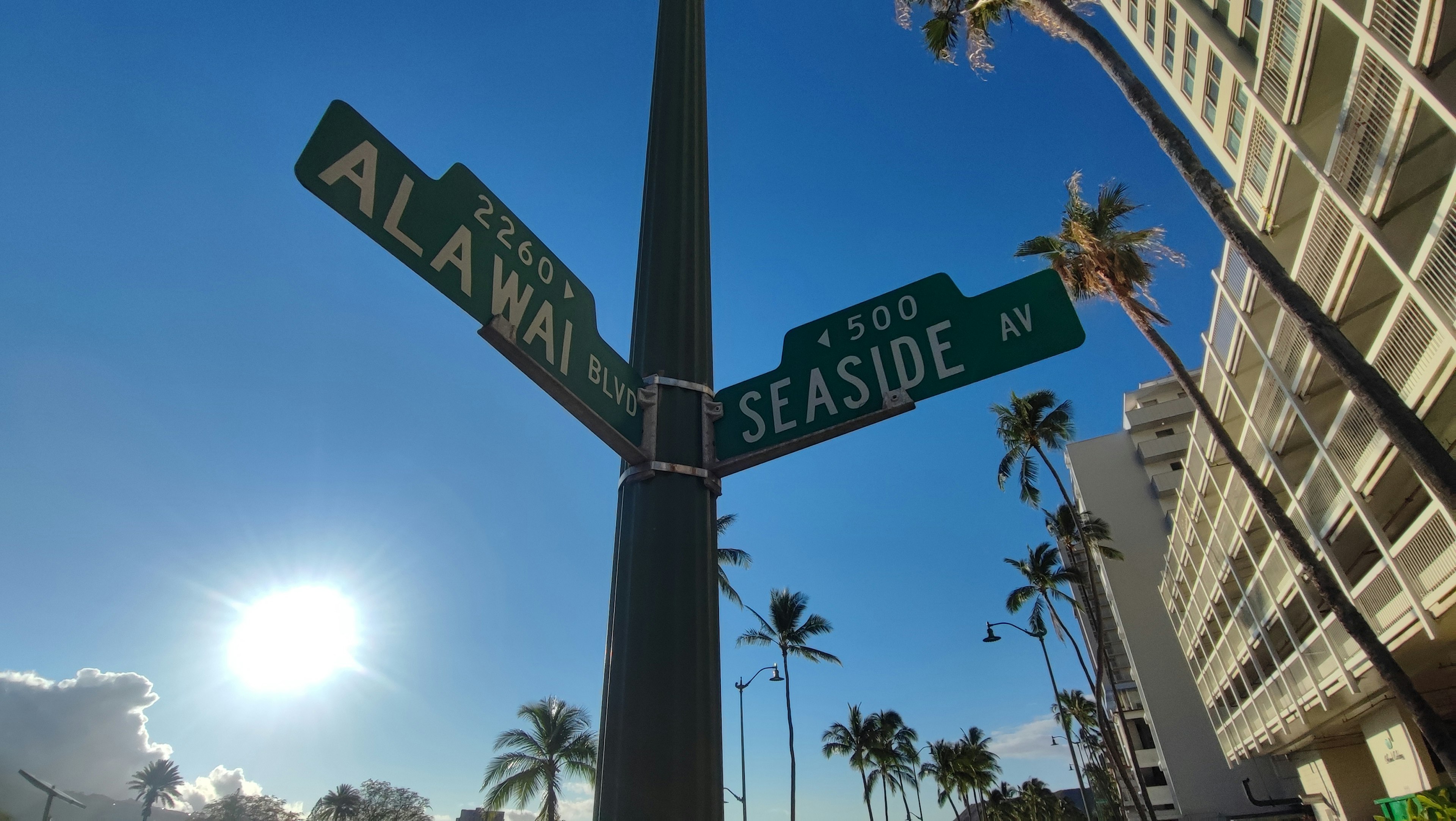 Señal de intersección de Alawai Street y Seaside Avenue con sol brillante en Hawái