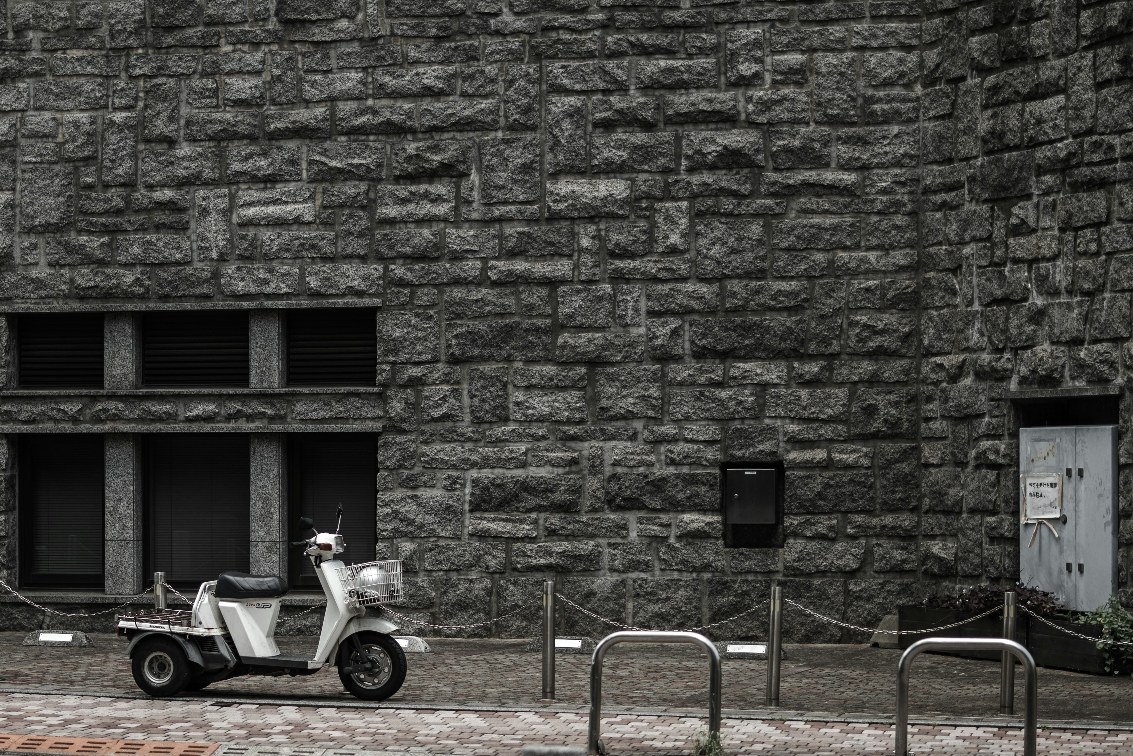 Un scooter blanc garé devant un mur en pierre grise