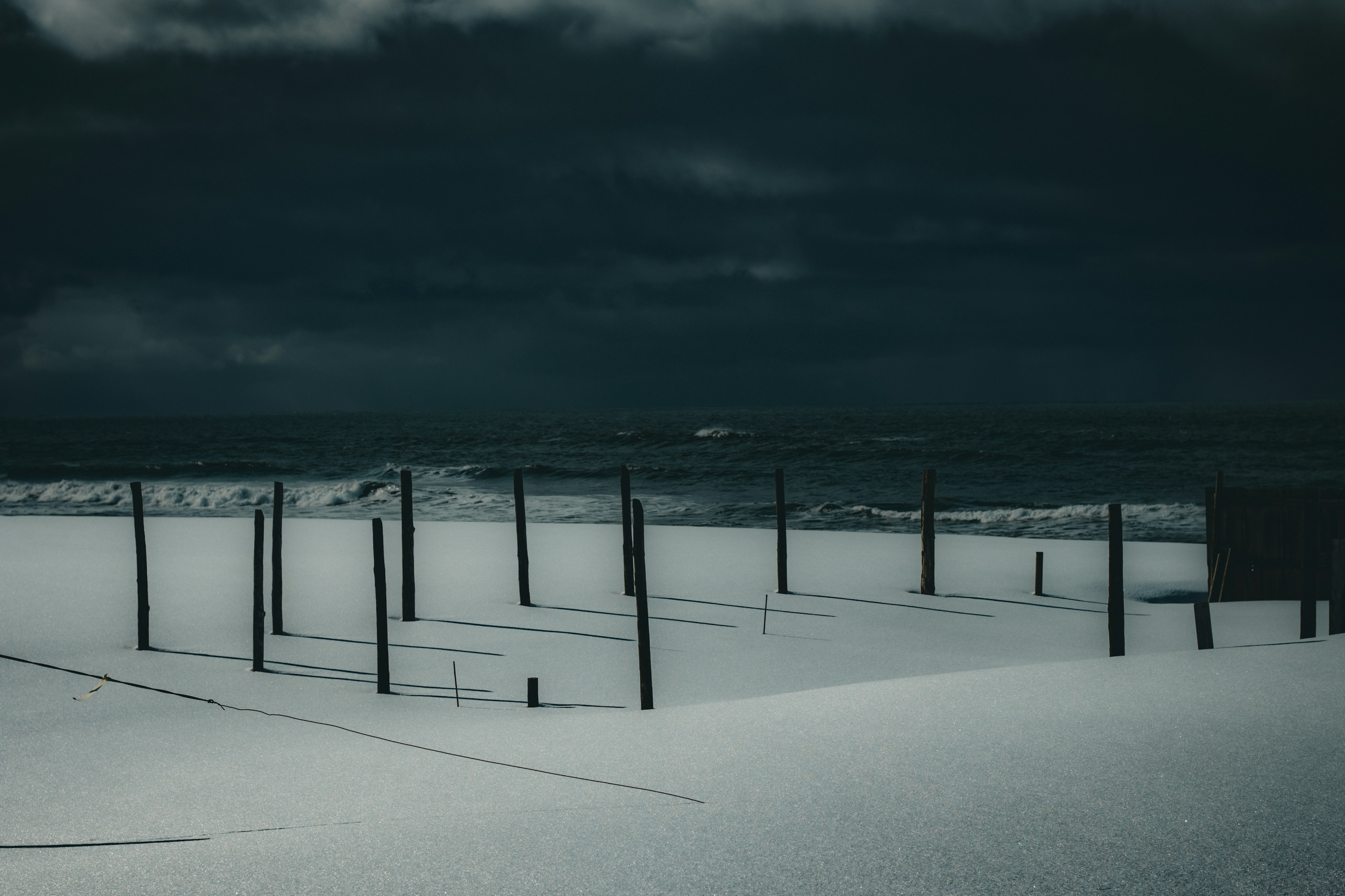 Dark ocean landscape with white sand and wooden posts standing