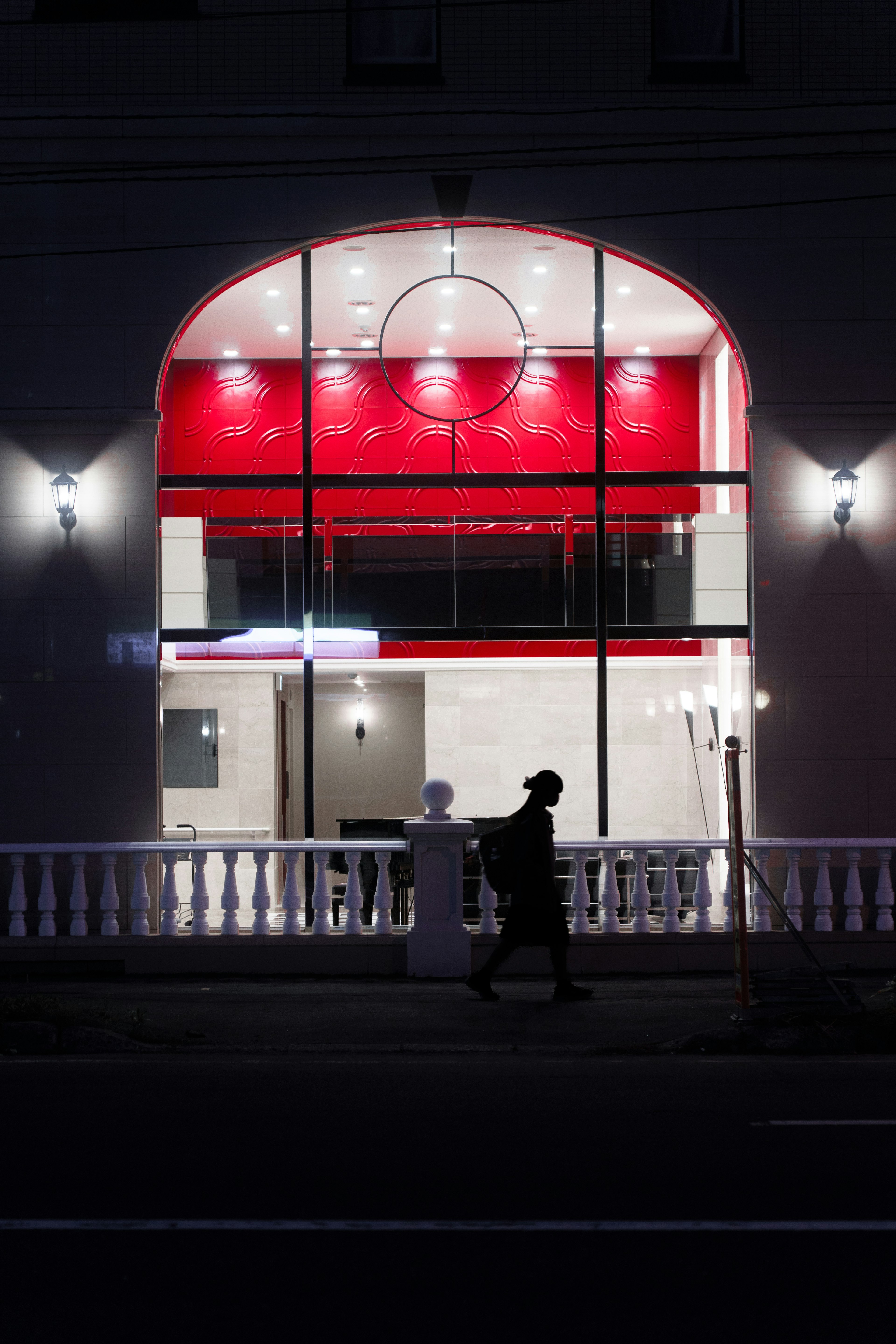 Silhouette d'une personne marchant devant un bâtiment avec des lumières intérieures rouges la nuit