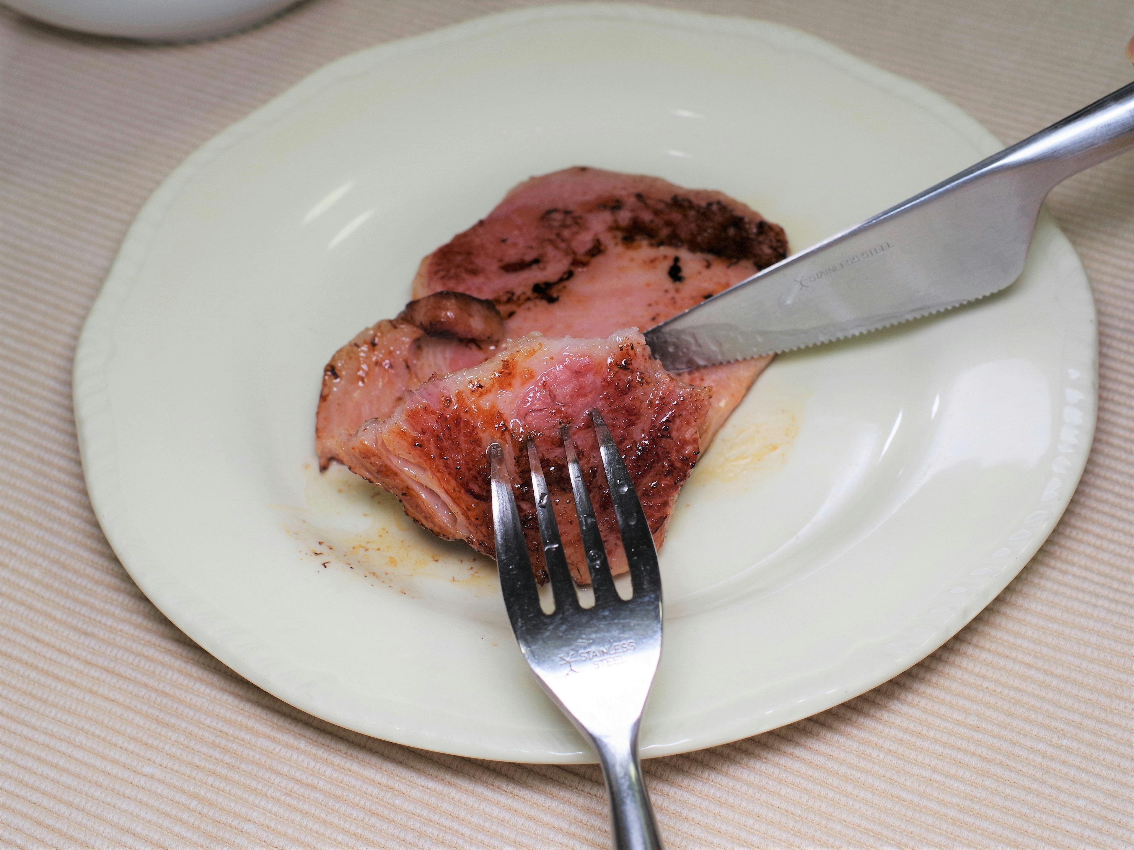 Geschnittenes Fleisch auf einem weißen Teller mit einer Gabel und einem Messer