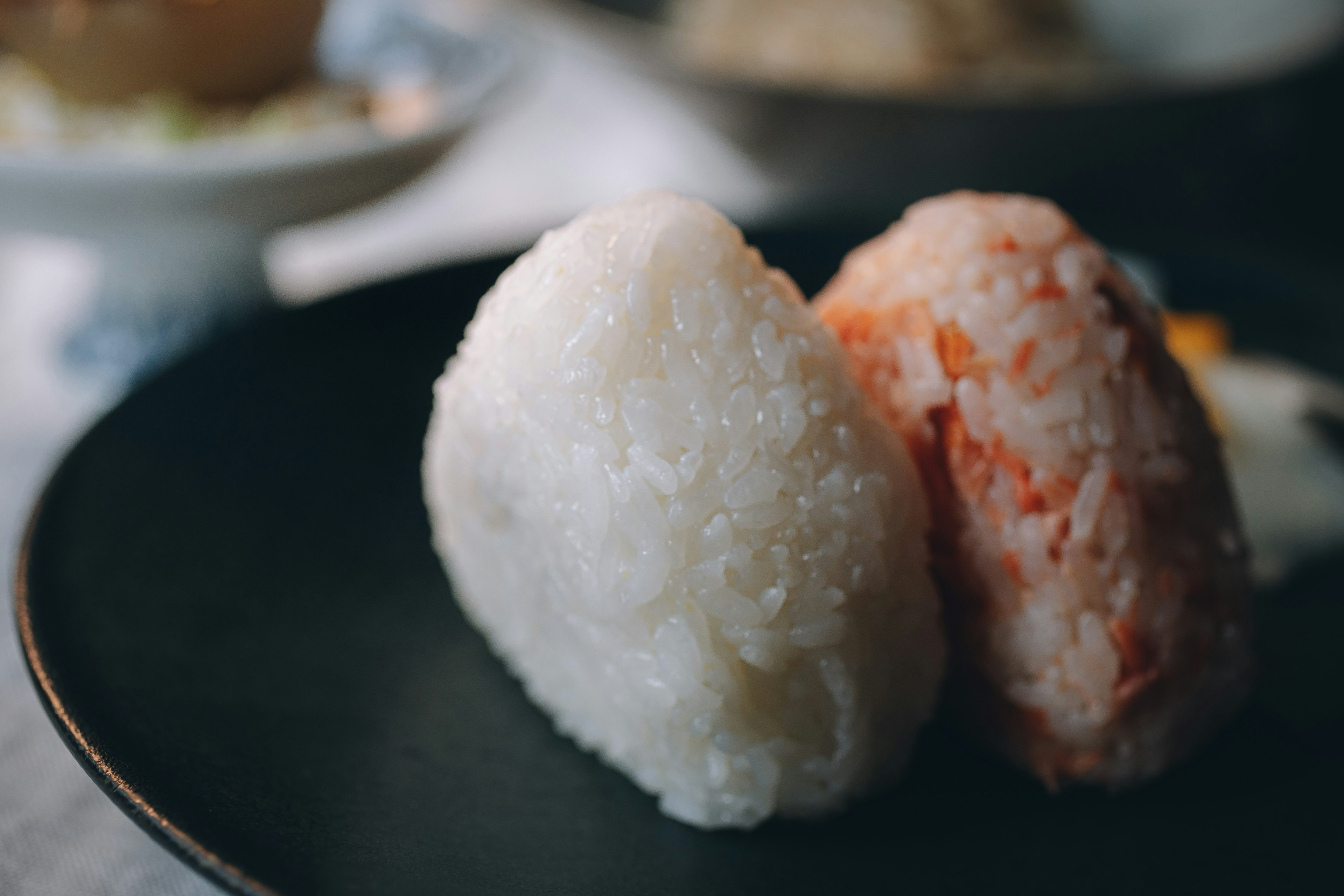 A black plate featuring rice balls one plain white and one salmon flavored