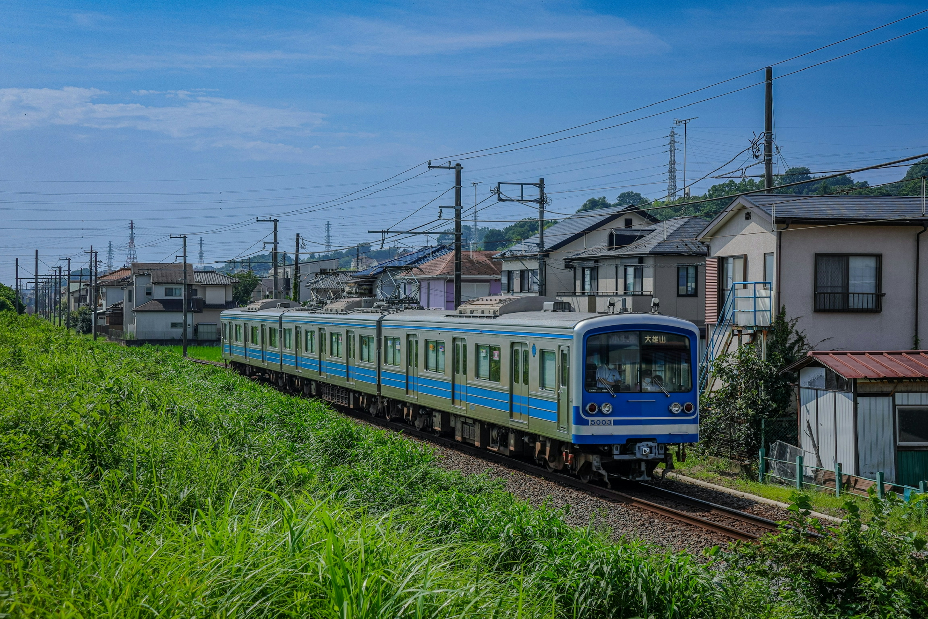 青い電車が住宅街を走る風景