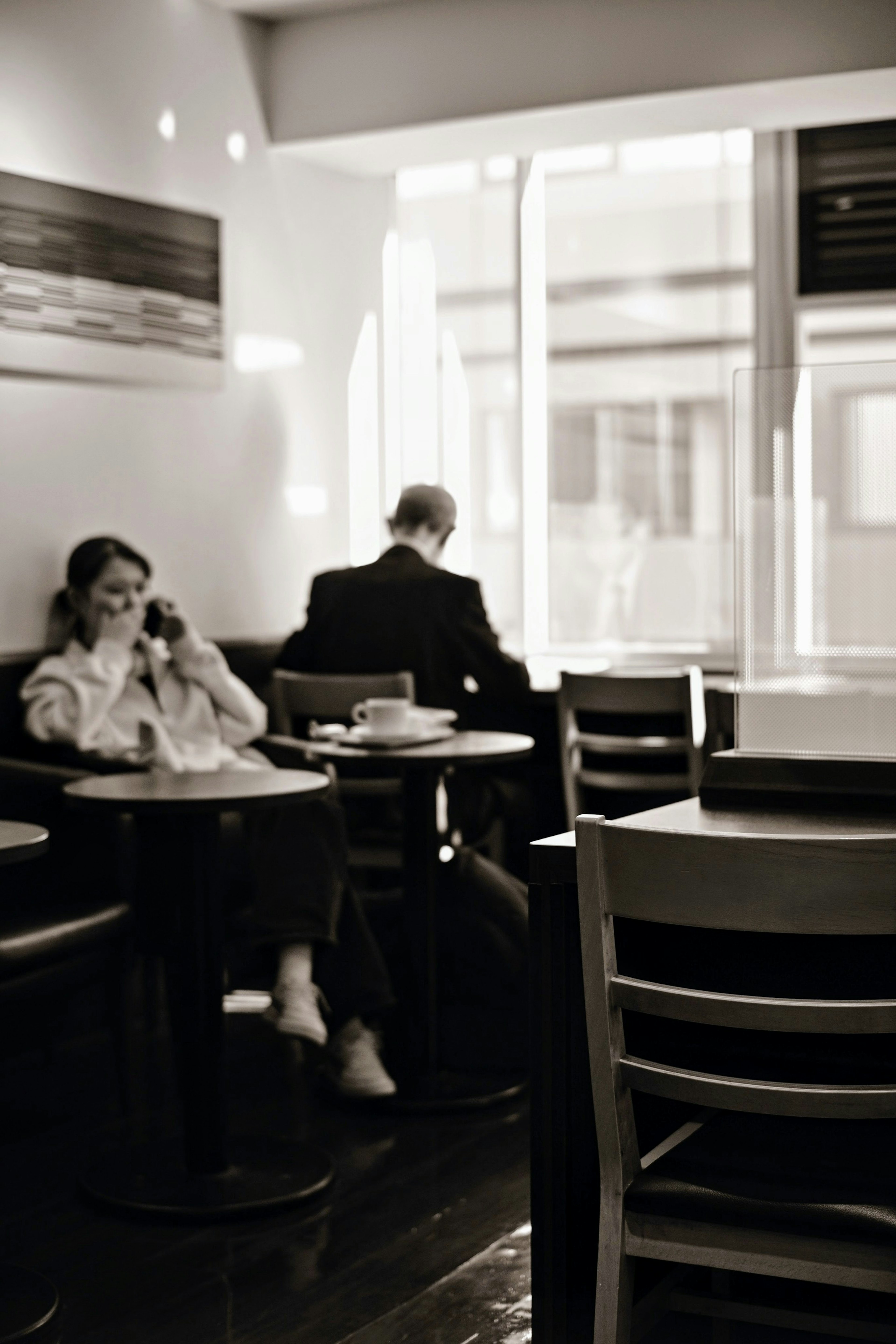 Black and white photo of a woman on the phone and a man sitting with his back turned in a cafe