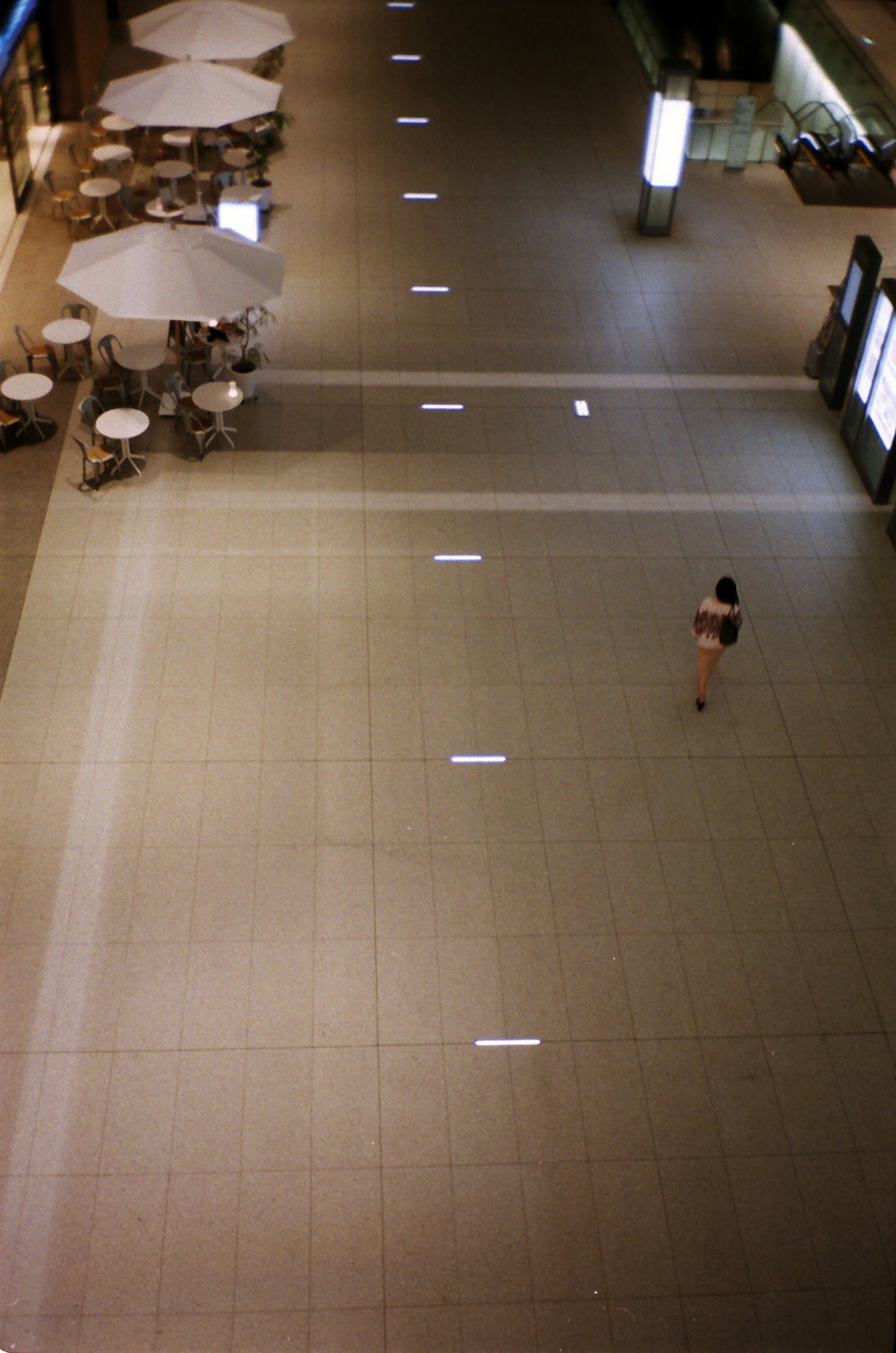 Vue aérienne d'un espace commercial moderne avec une personne marchant Sol en carreaux lumineux et zones de sièges visibles