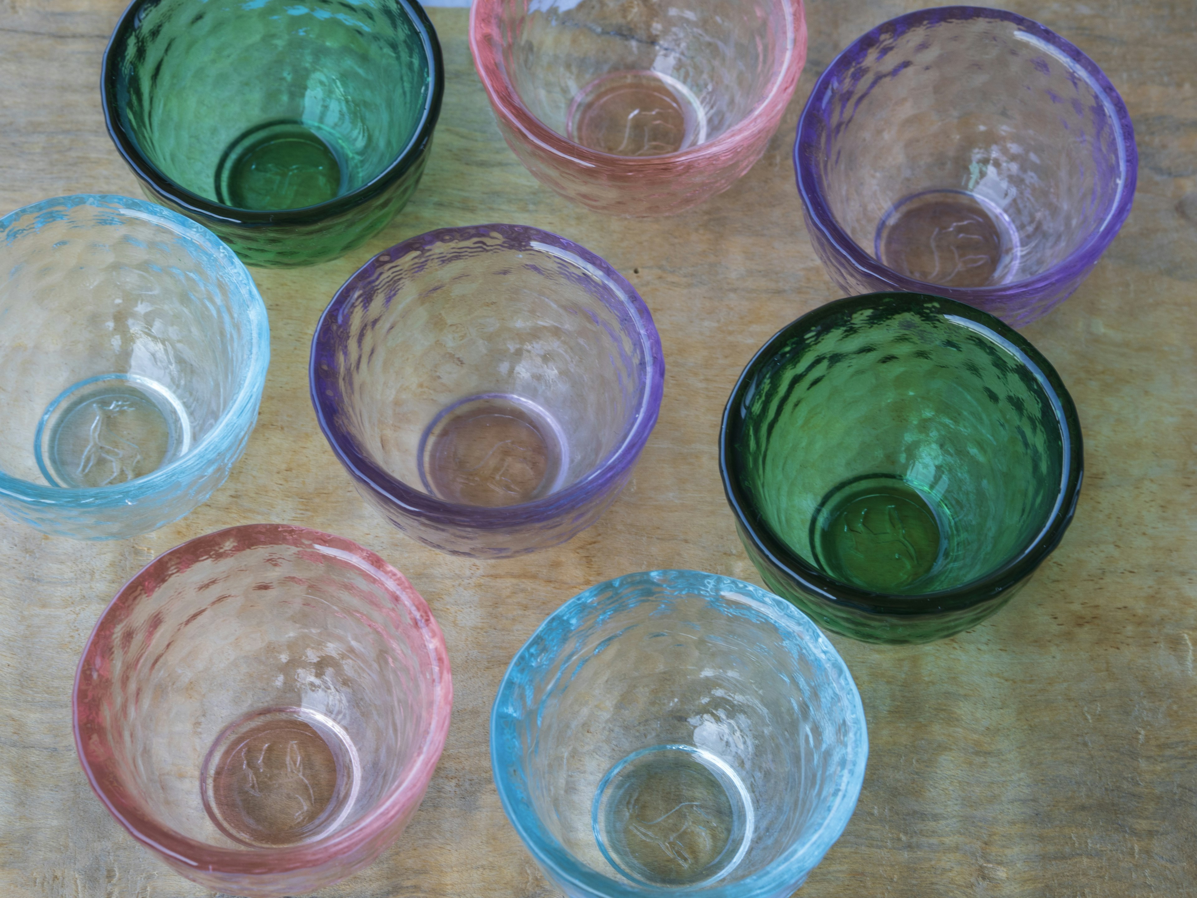 Eight colorful glass bowls arranged on a wooden surface