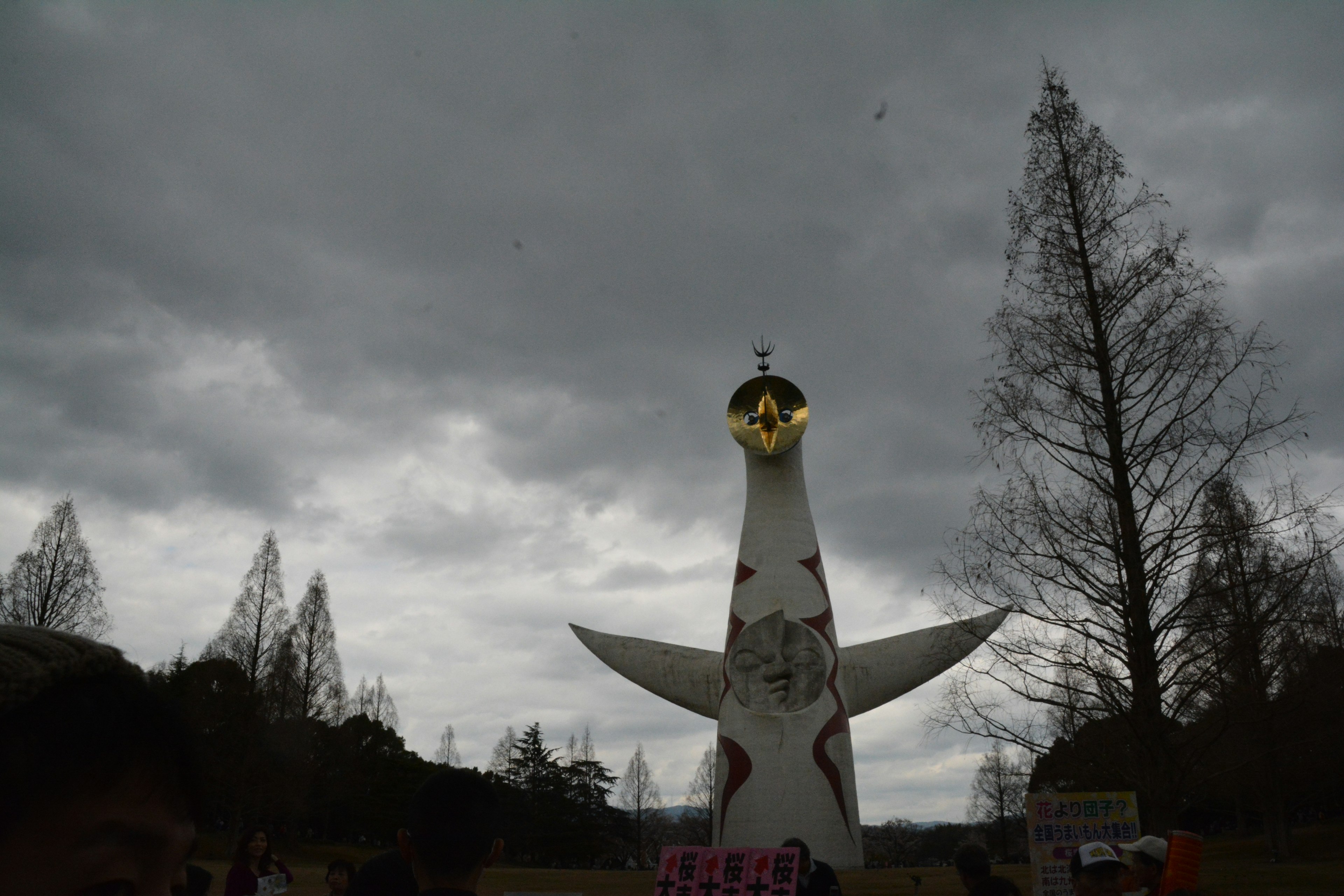 A large white sculpture stands under a cloudy sky surrounded by trees