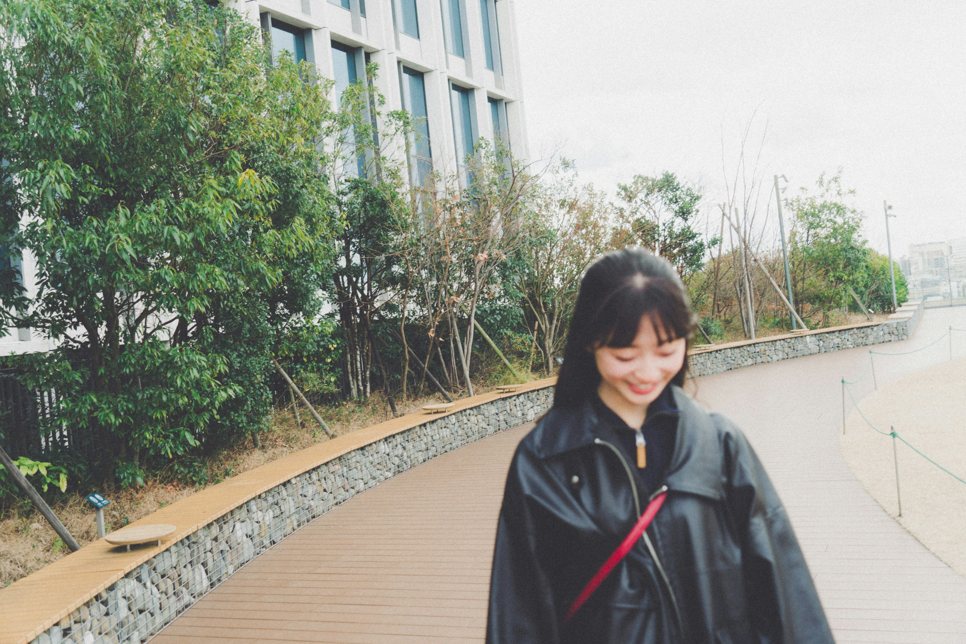 Mujer con impermeable negro sonriendo en un entorno exterior pintoresco