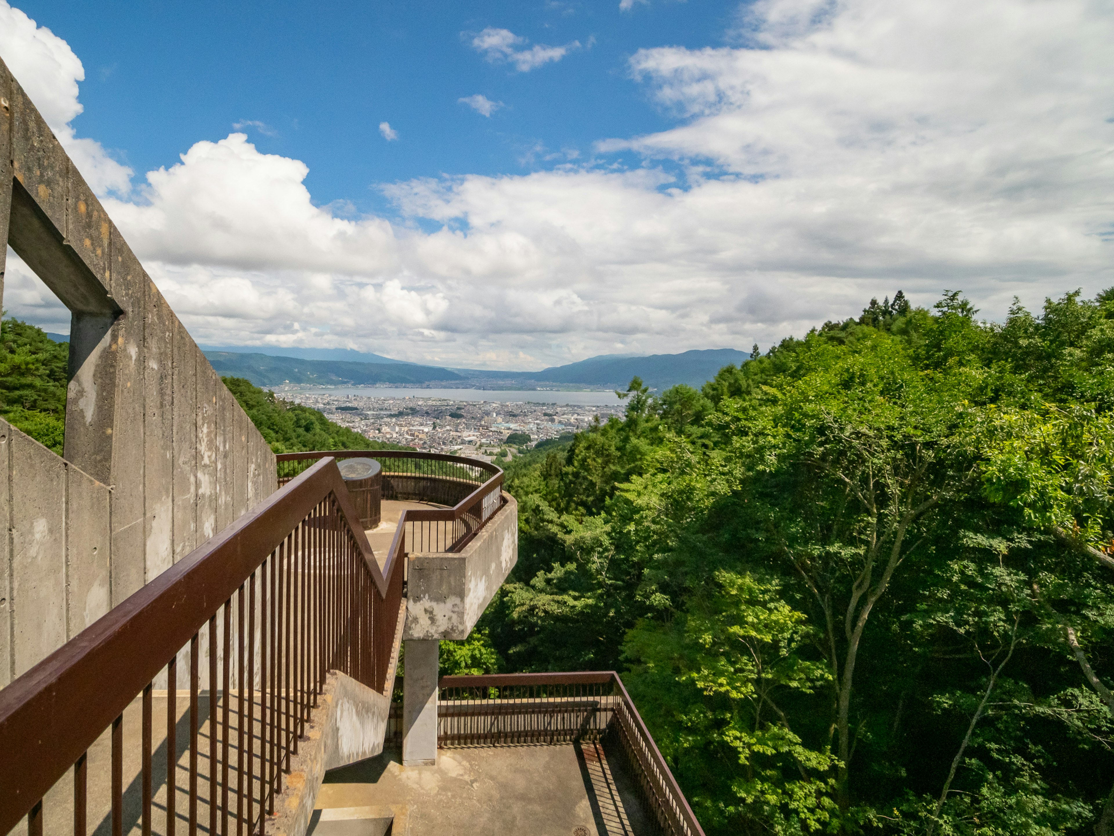 Escaliers d'une plateforme d'observation avec des montagnes verdoyantes et un ciel bleu