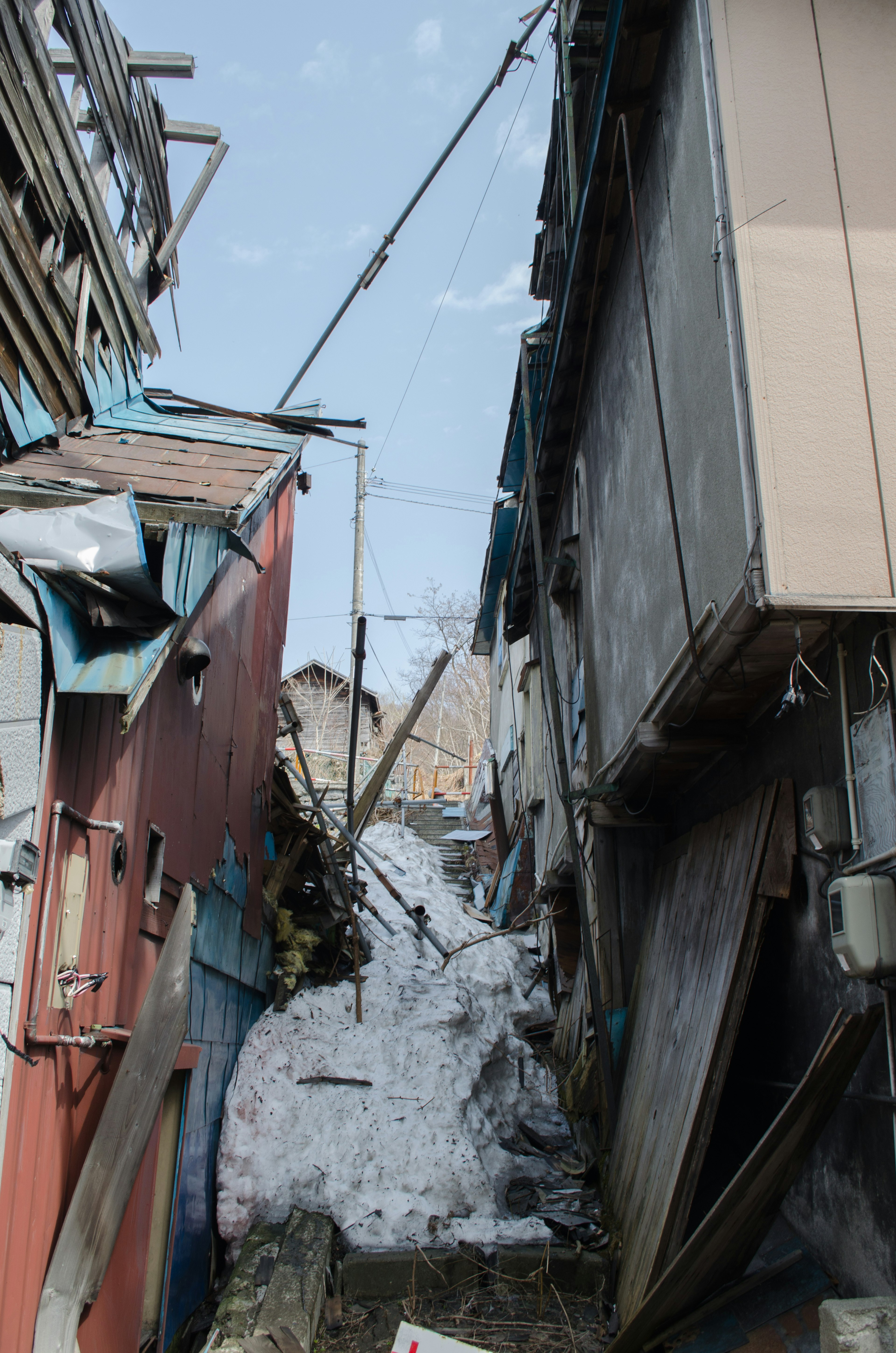 Narrow path between collapsed buildings with snow accumulation