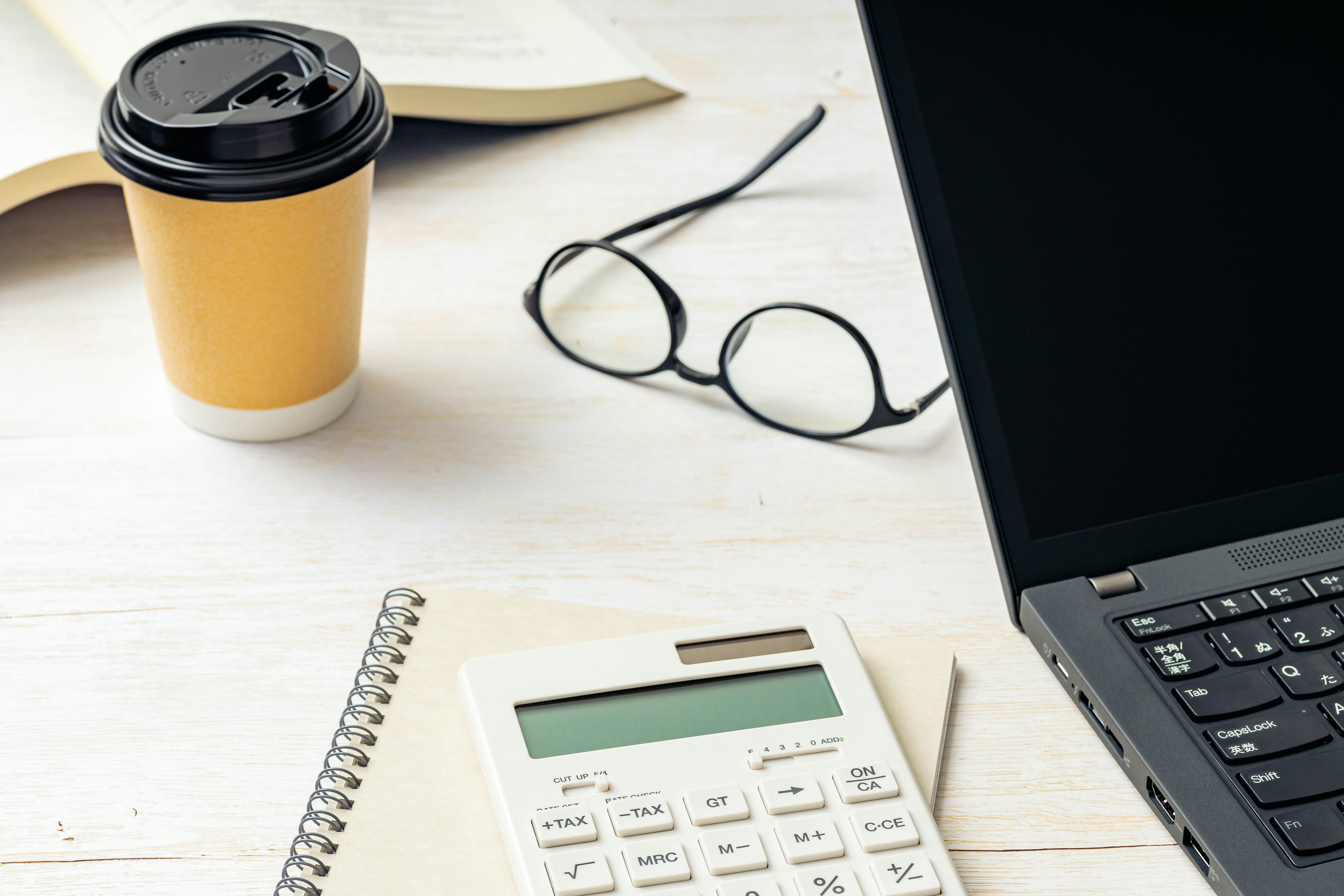 Un ambiente di lavoro semplice con laptop, calcolatrice, tazza di caffè e occhiali su una scrivania